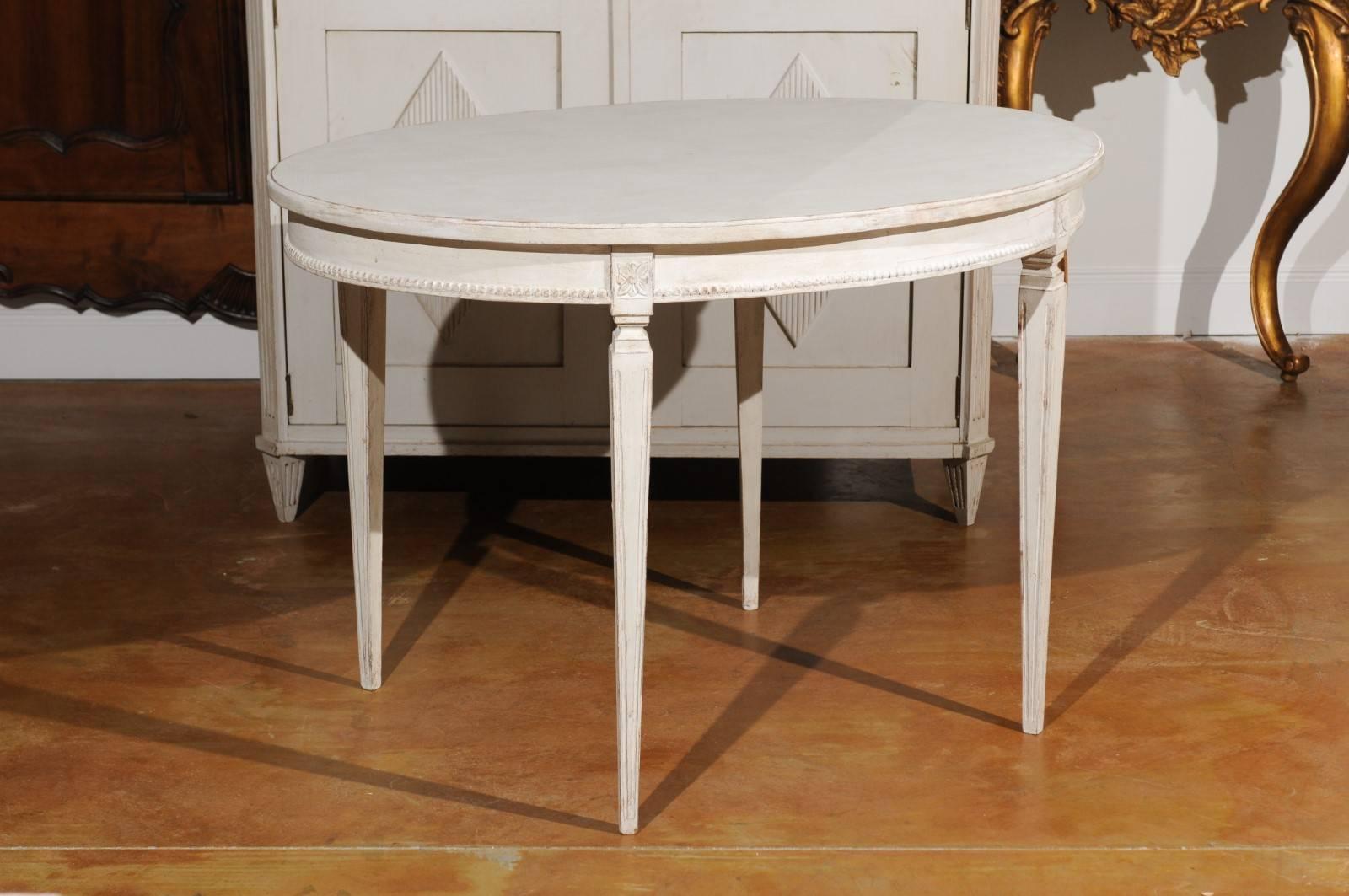 A Swedish Gustavian style early 20th century painted oval table from Växjö. Born in the southern town of Växjö in the Kronoberg County, this Swedish painted table features an oval top sitting above an elegant apron, delicately accented with beaded
