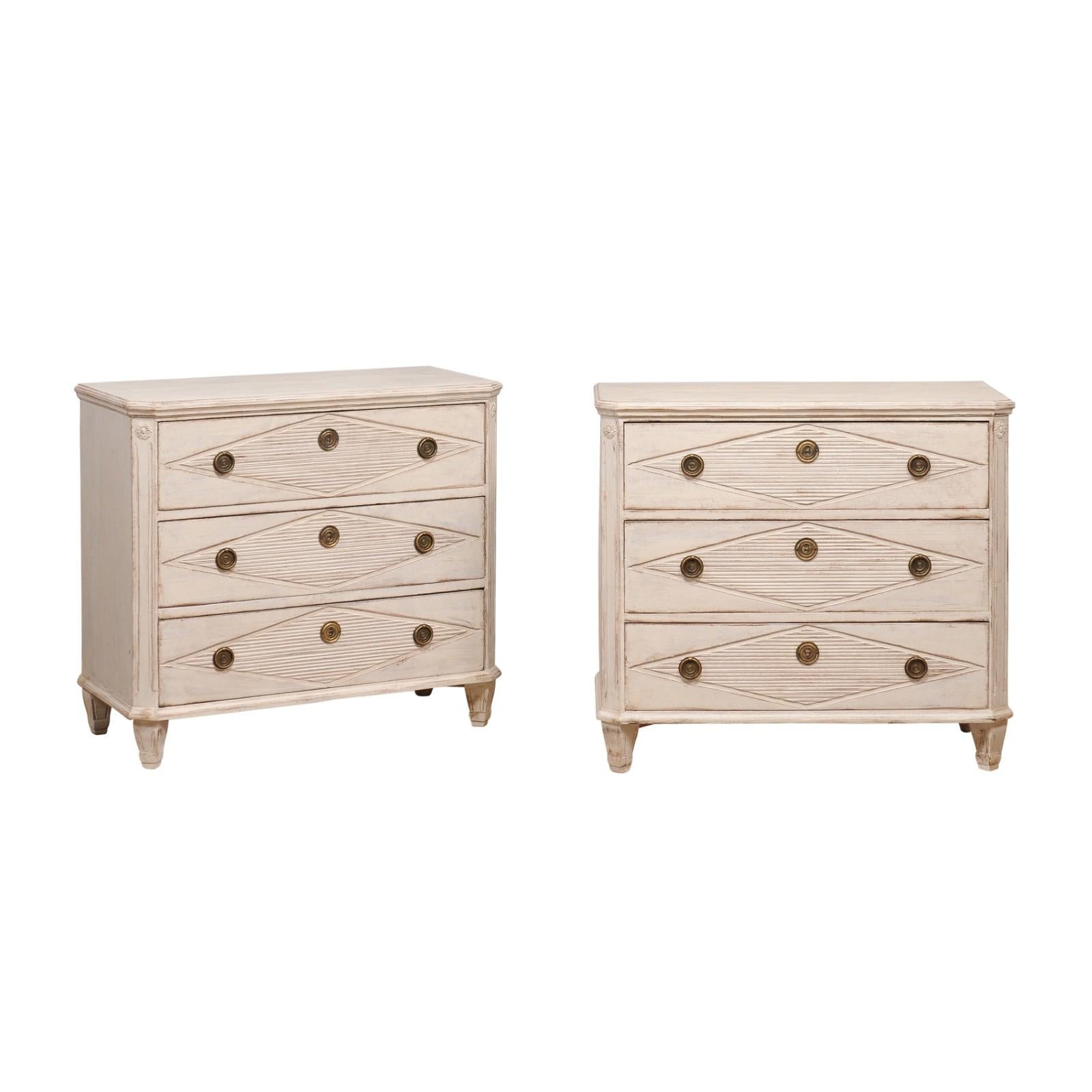 A pair of Swedish Gustavian style painted wood chests from the 19th century with three drawers each, carved reeded diamond motifs, canted side posts and tapered feet. This stunning pair of Swedish Gustavian style painted wood chests, hailing from
