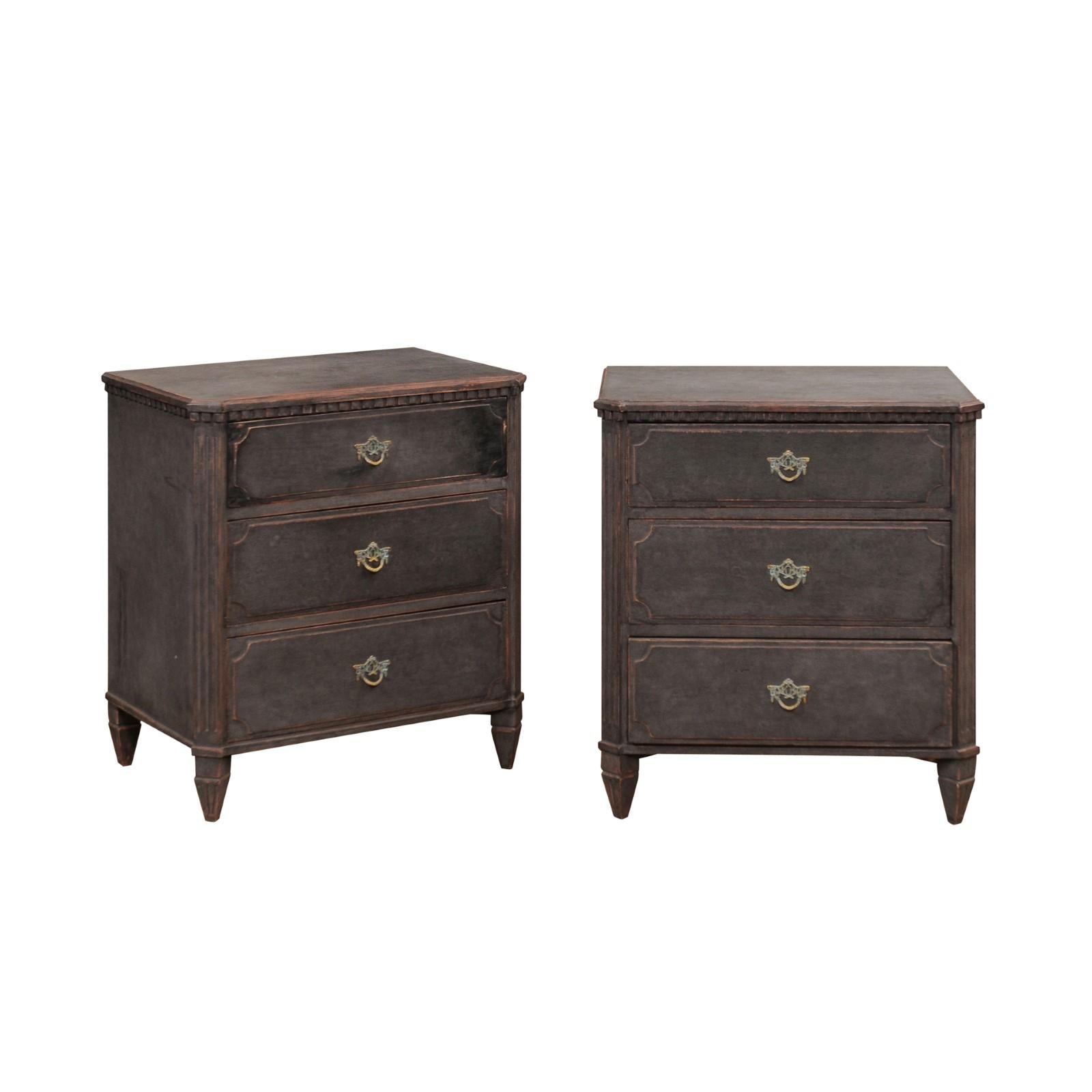 A pair of Swedish Gustavian style chests from the 19th century with antique charcoal / black painted finish, three drawers, carved dentil molding and canted side posts. This pair of Swedish Gustavian style chests from the 19th century exudes a