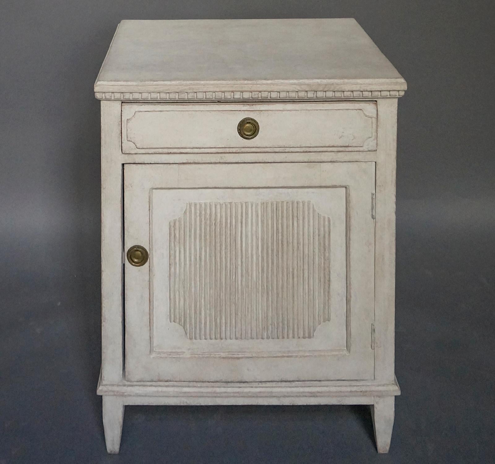 Half-height cabinet, Sweden circa 1870, in the Gustavian style with a single drawer over a full width door. Shaped top with dentil molding. Both the drawer and the door feature raised panels, with the door having vertical reeding. Single fixed shelf