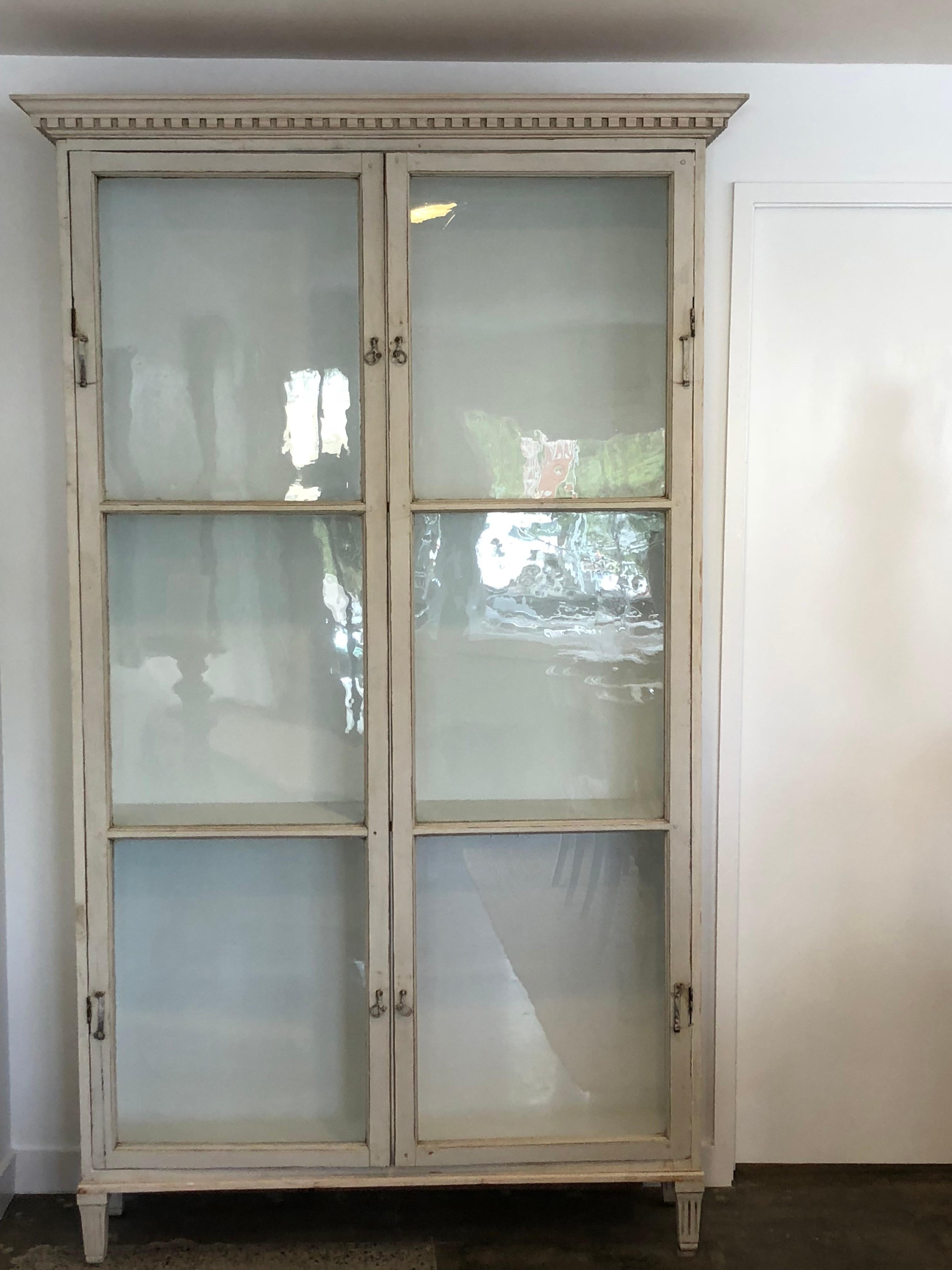 This gorgeous cabinet features antique glass doors that were previously windows on a Swedish structure. The inside of the doors have a lovely authentic patina. The front of the doors retains the metal latches that would have securely fastened the