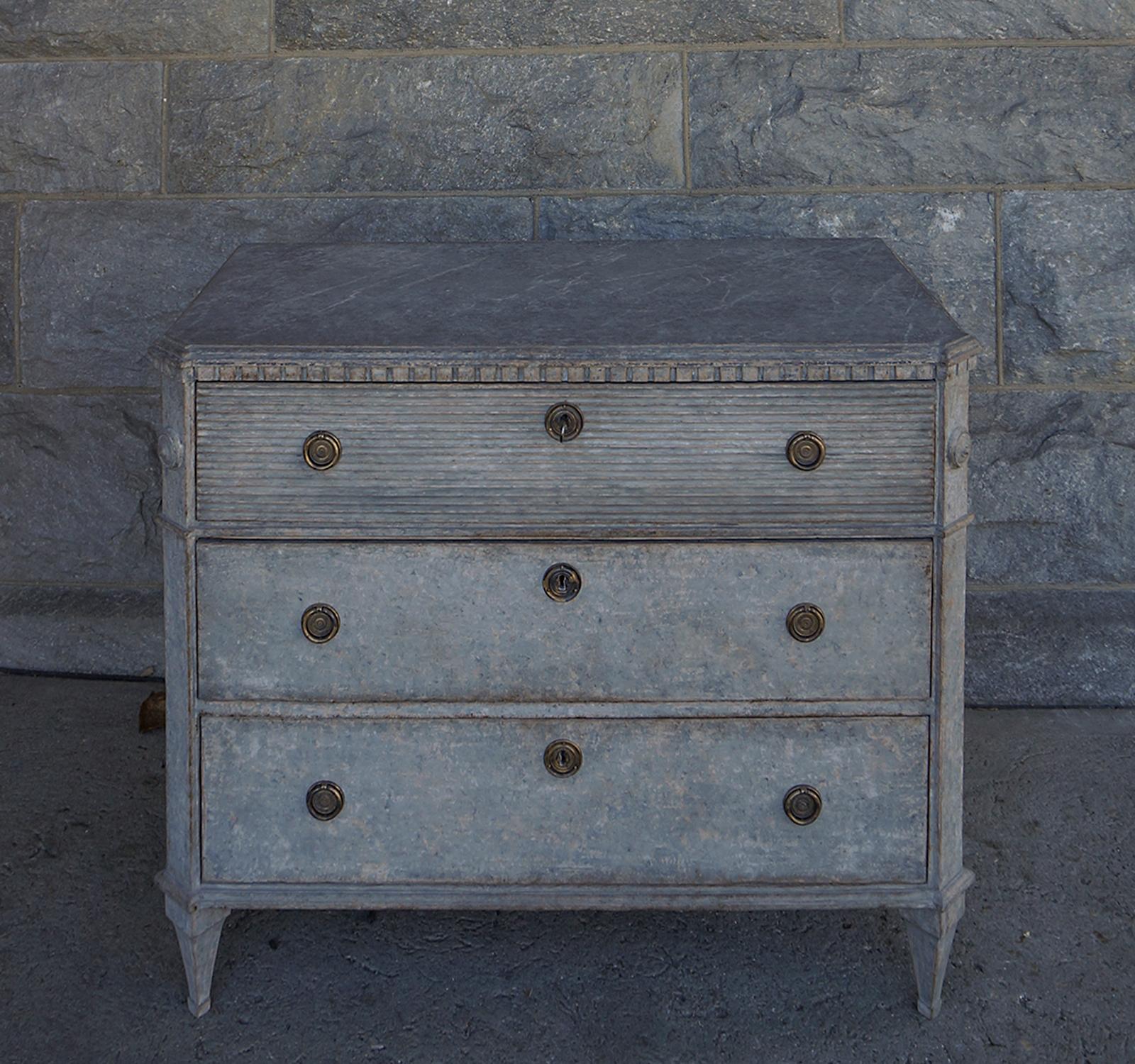 Swedish chest of drawers, circa 1870, in the Gustavian style. Shaped top with marbled paint and dentil molding. Canted corners with applied rondels at the top and tapering square feet at the bottom. Horizontal fluting across the top drawer front. No