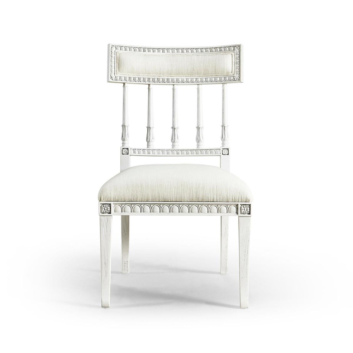 A Swedish Neo-Classic Gustavian style dining chair, with a chalky white painted finish, carved upholstered top rail about turned acanthus wrapped plates, with a box cushion seat raised on flared legs. 

Dimensions: 21.25