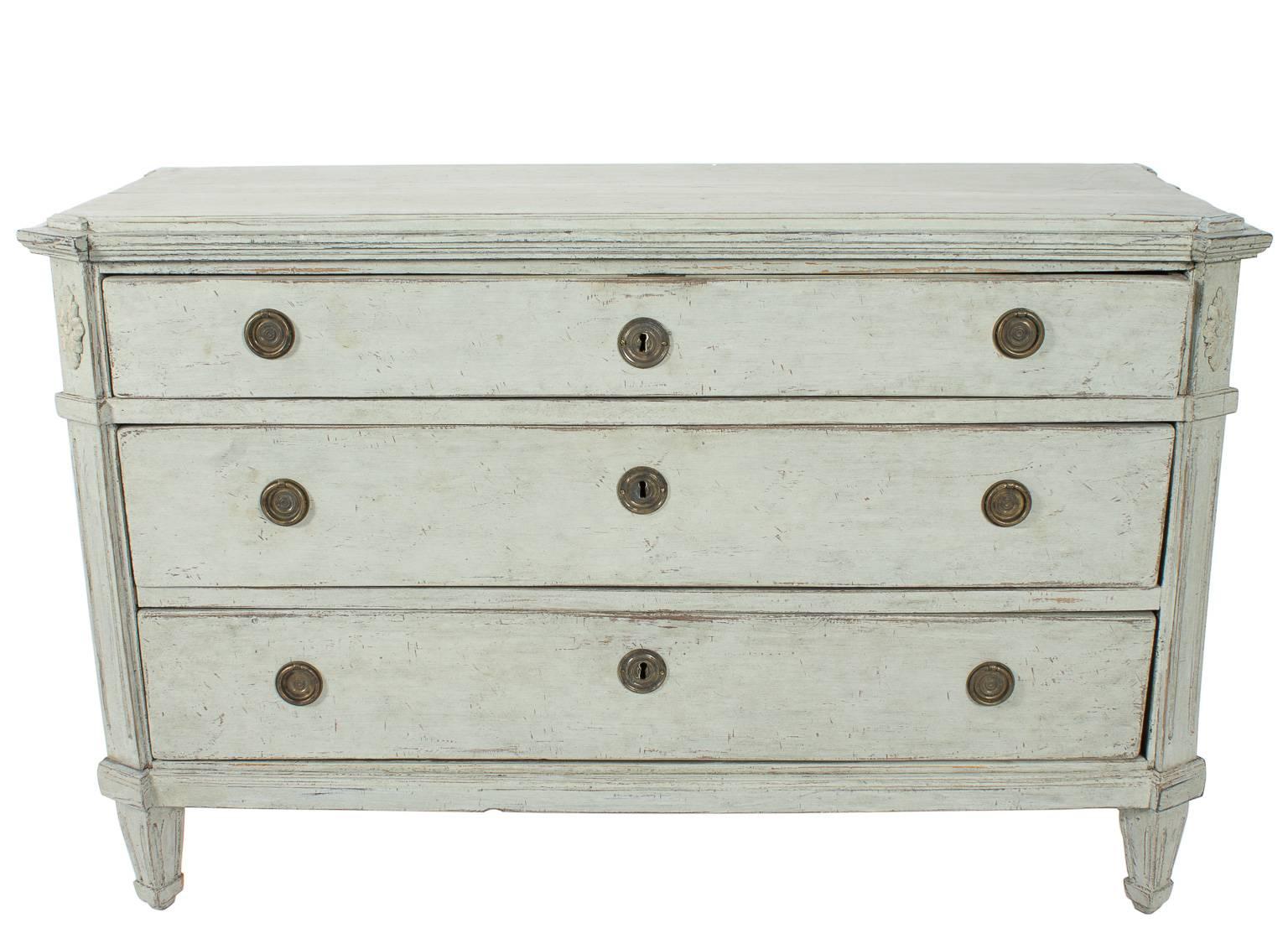 Late 19th century Swedish white-painted Gustavian-style dressers. Each with floral fluted detailing, three drawers, and brass fittings.