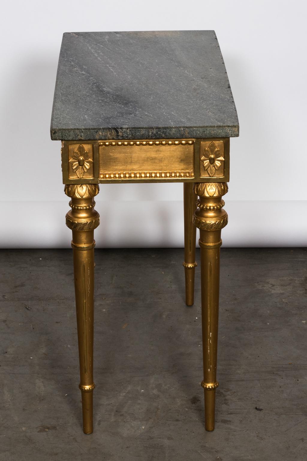 Gustavian style console table with dark stone top and gilded and bronzed wood base, circa late 19th century. The console also features carved beaded trim, rosettes, and arrow turned legs.