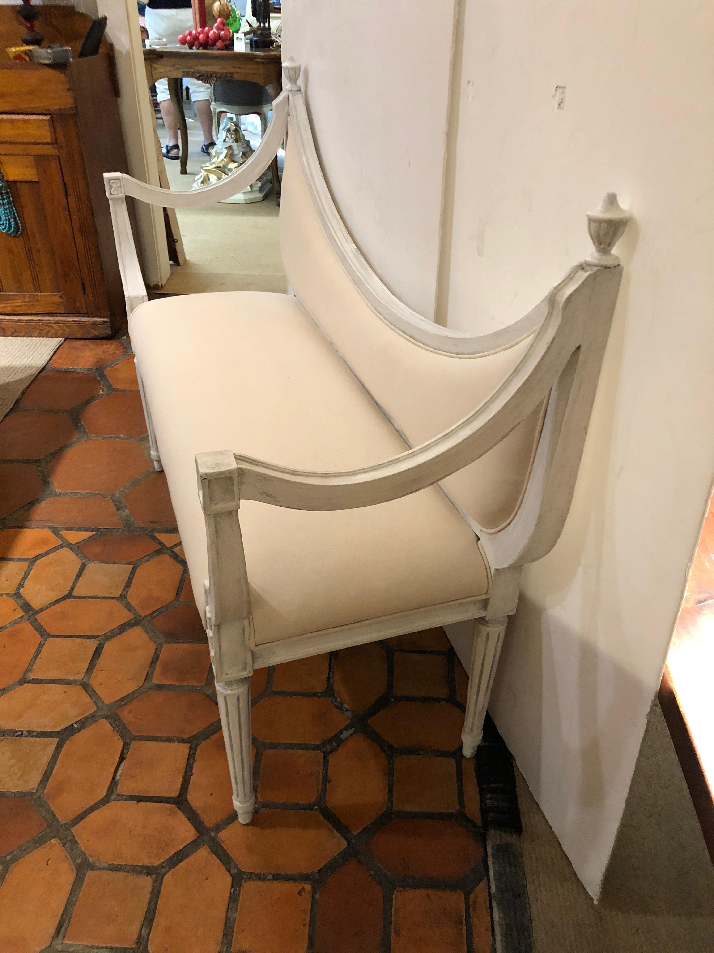 Dreamy scoop back settee bench with grayish white painted wood, reeded legs and wonderfully shaped arms, urn shaped finials, newly upholstered in white duck.

Measures: Seat height 17.