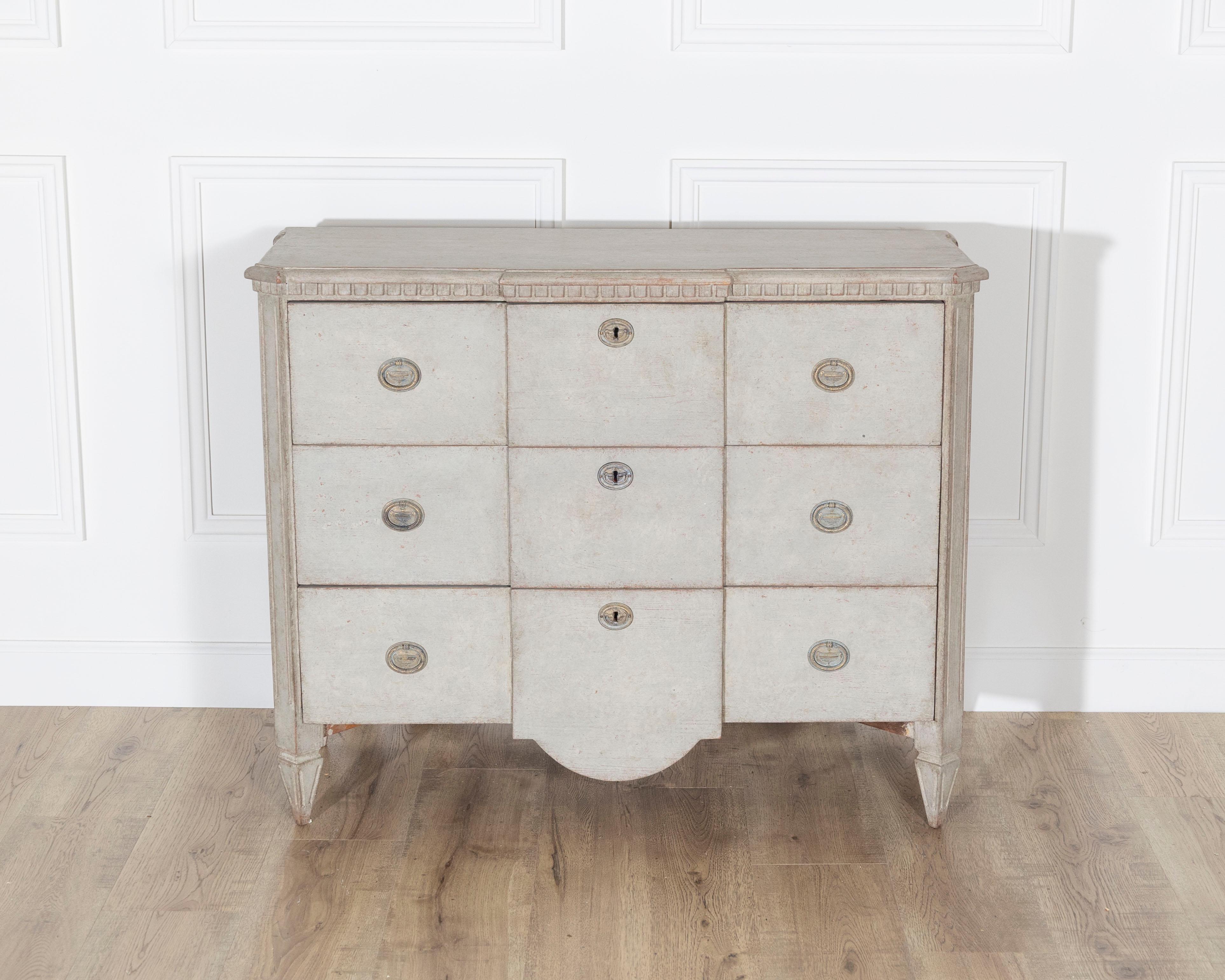 Cette commode de style gustavien est un exemple raffiné du design néoclassique suédois. Elle est fabriquée en pin et recouverte d'une peinture grise douce qui rehausse son attrait intemporel. La poitrine présente un profil à front brisé, ce qui