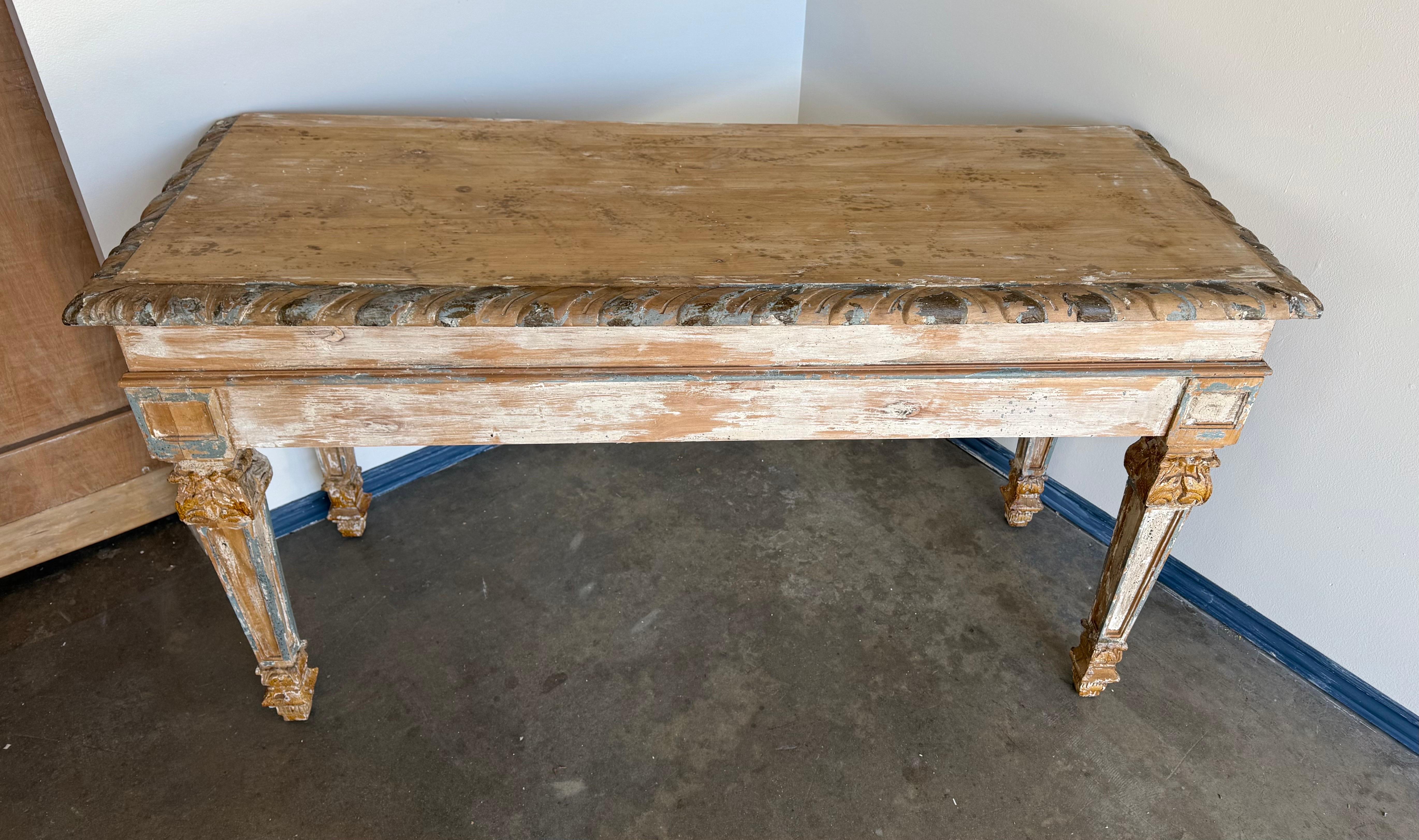 This painted console table exudes rustic elegance with its distressed finish and classical lines. The wood surface shows layers of worn white paint, exposing hints of the natural wood and traces of soft blue and gold accents, lending it a timeworn,