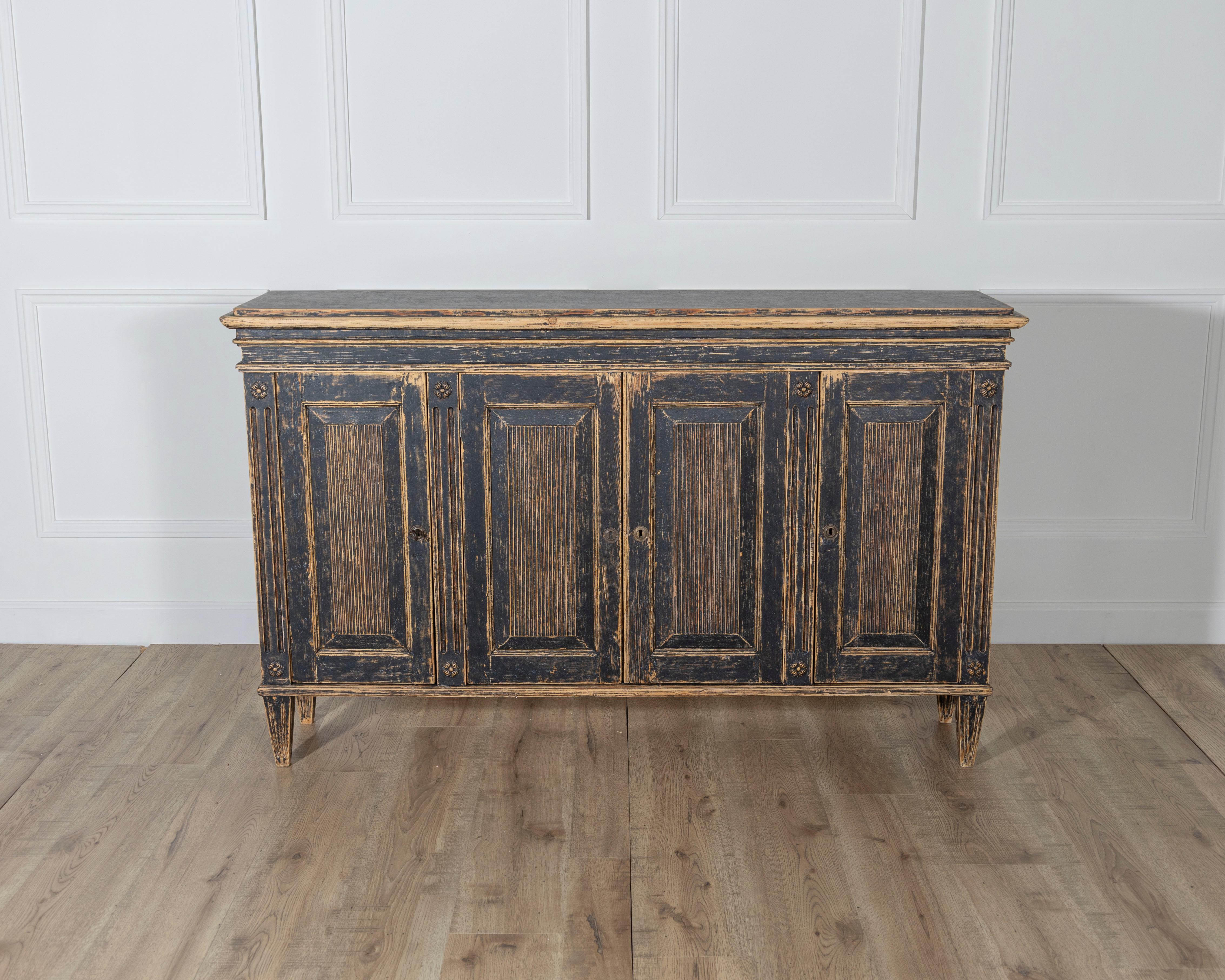 A stately Gustavian-style sideboard from Sweden, likely dating to the early 20th century. This piece features four paneled doors, each adorned with vertical reeded detailing, a hallmark of the Gustavian aesthetic that brings rhythm and texture to