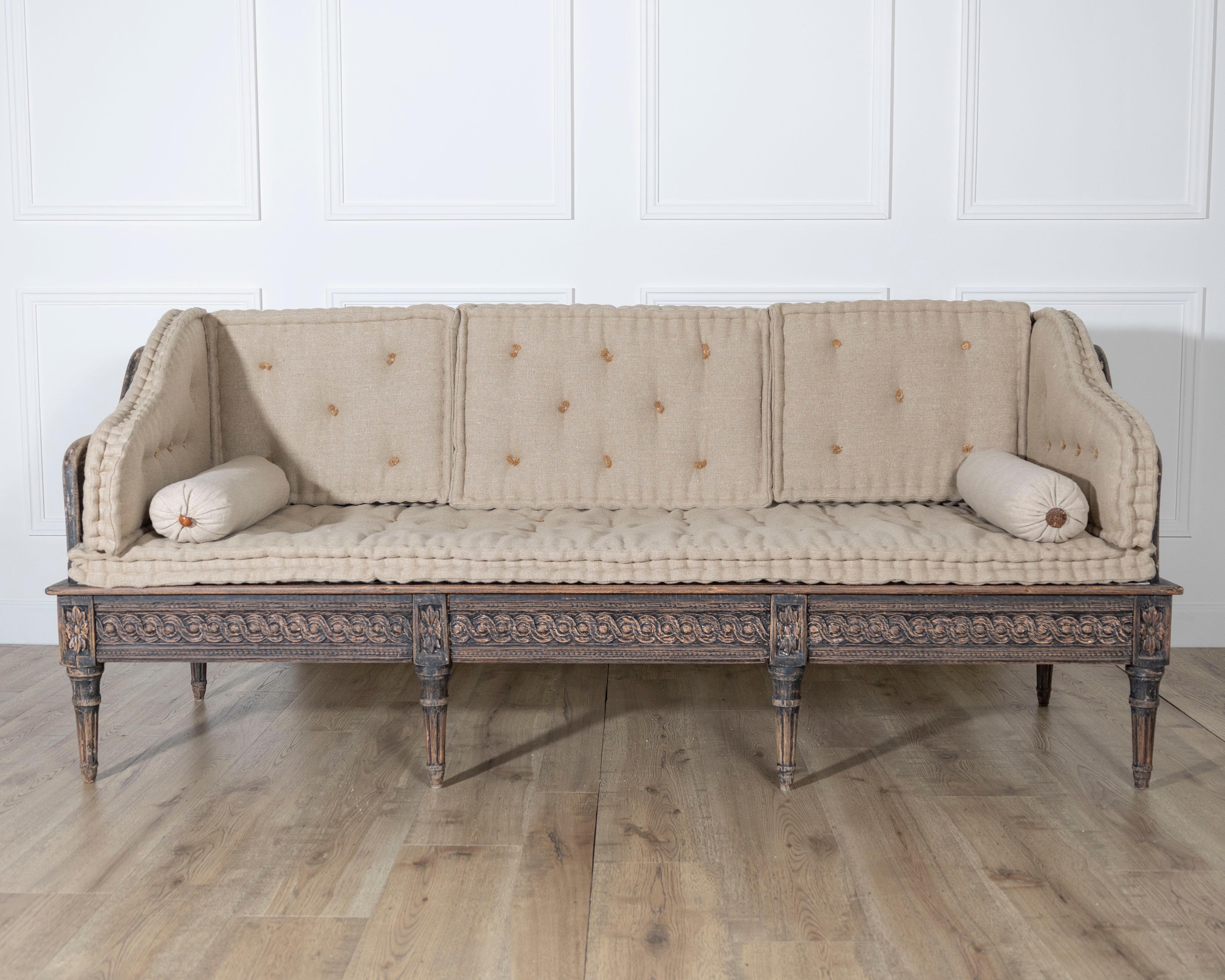 A graceful Gustavian style trågsofa from Sweden, dating to circa 1920. This piece features a painted black wooden frame with richly carved apron and legs, exhibiting the neoclassical influence that defines Gustavian design. The bench-like