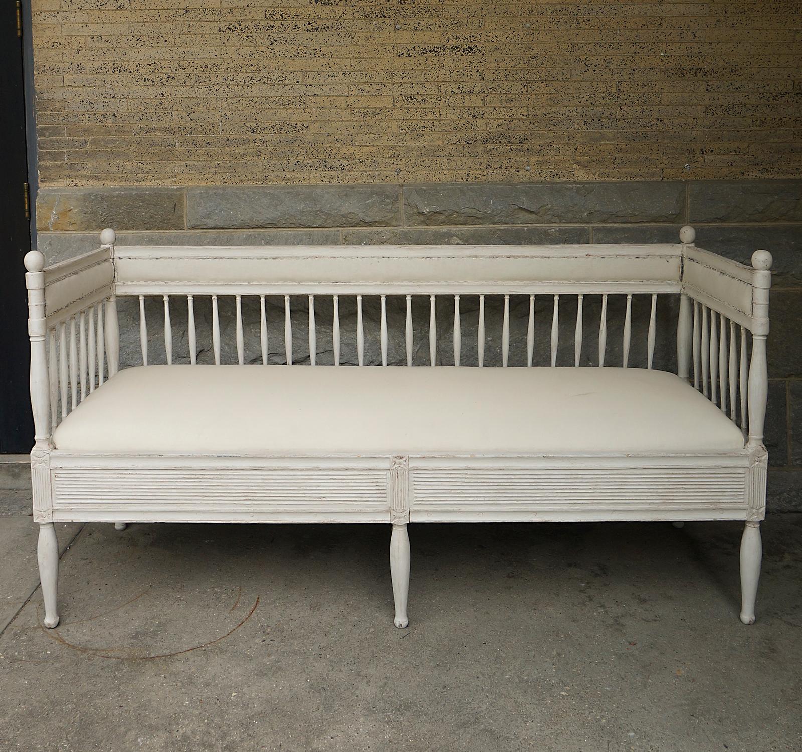 Swedish sofa in the Gustavian style, circa 1850, featuring hand-turned spindles below narrow upholstered panels on the back and sides. The upholstered slip seat fits snugly into reeded panels with carved rosettes above the turned legs.