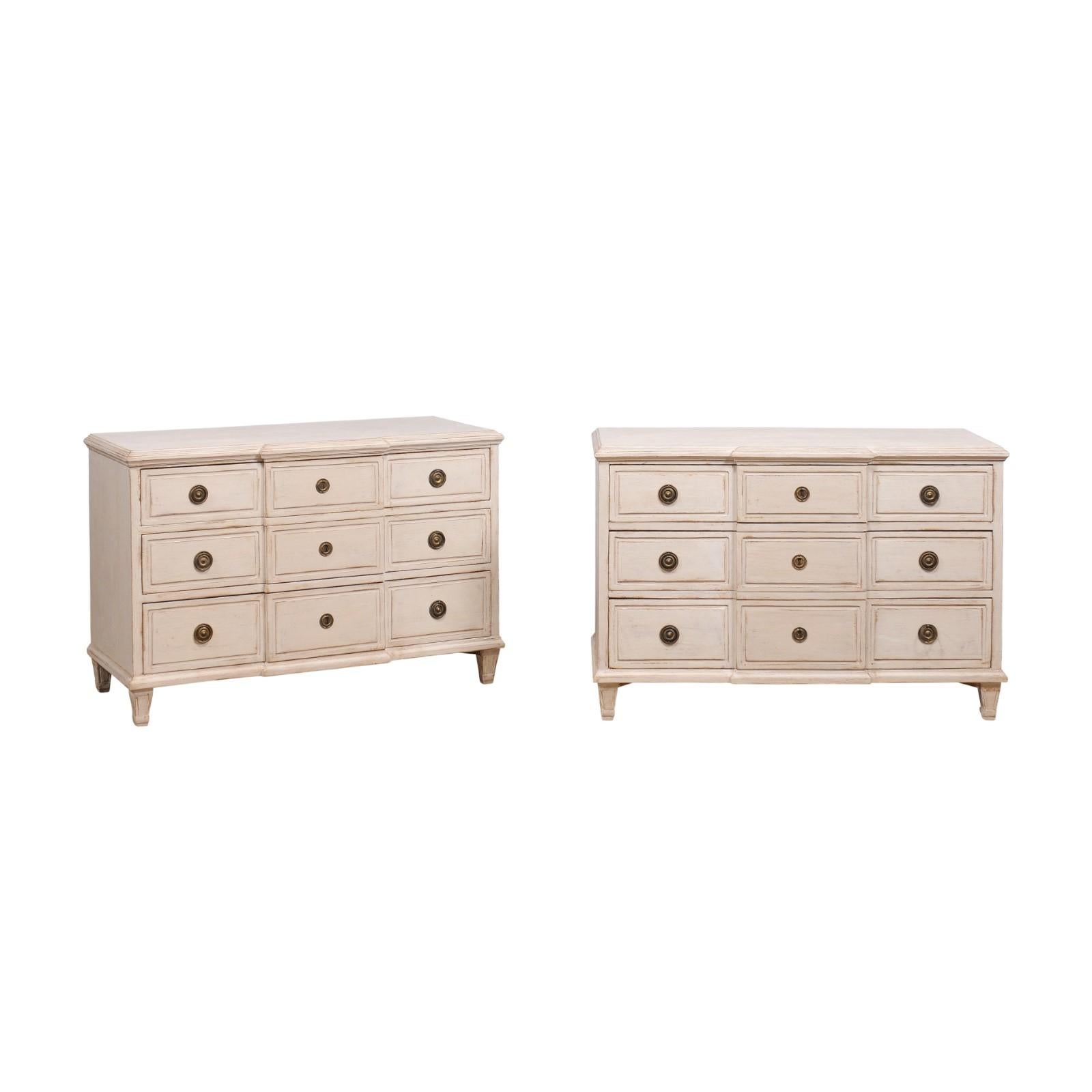 A pair of Swedish Gustavian style breakfront chests from the 20th century with off white / beige painted finish, three drawers, tapered feet and brass hardware. This exquisite pair of Swedish Gustavian style breakfront chests exudes timeless