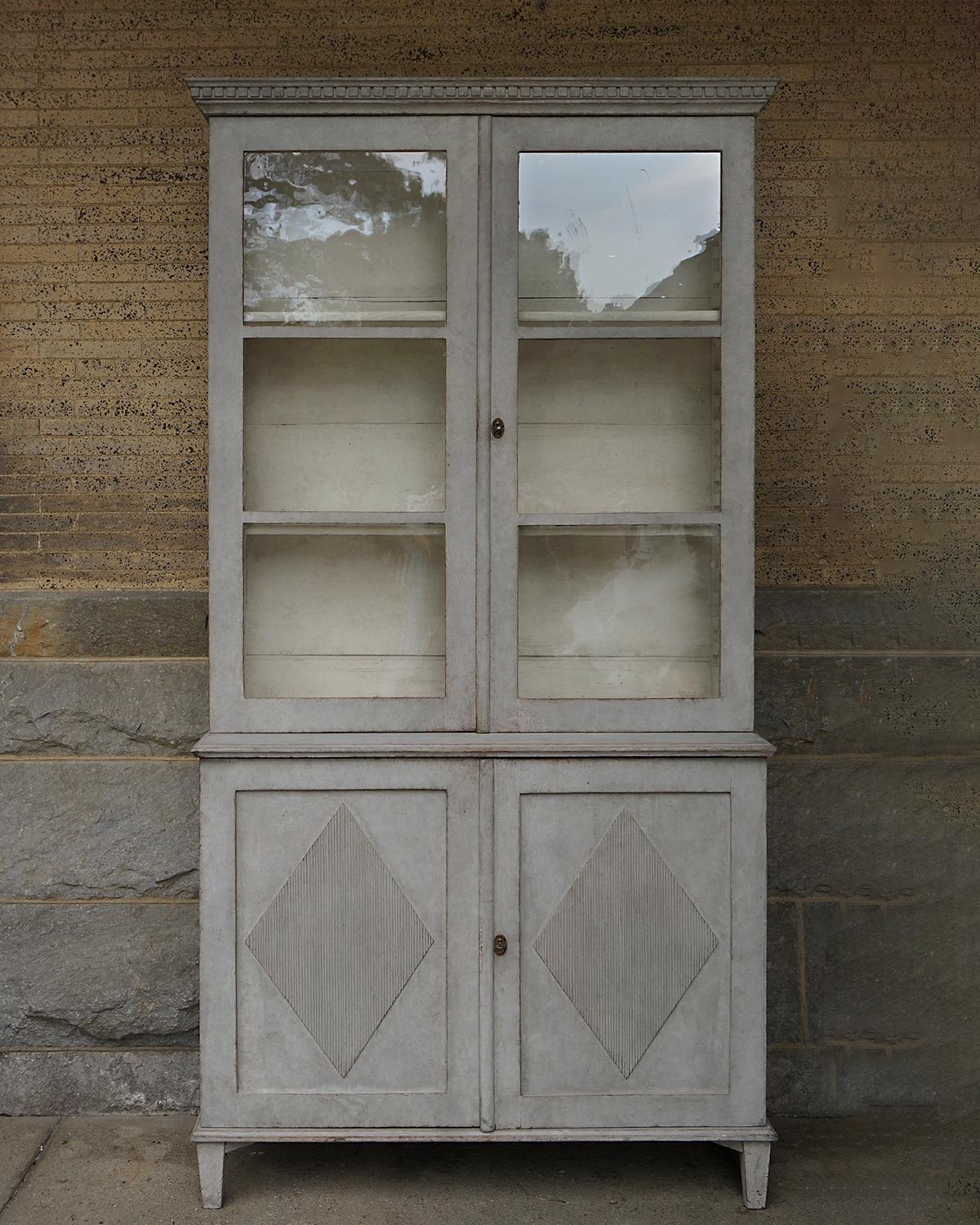 Swedish cabinet with glass doors in the late Gustavian Style, circa 1850. The upper section has two moveable shelves behind double doors, all under a cornice with dentil detail. The lower section has a pair of doors with raised, reeded panels and a