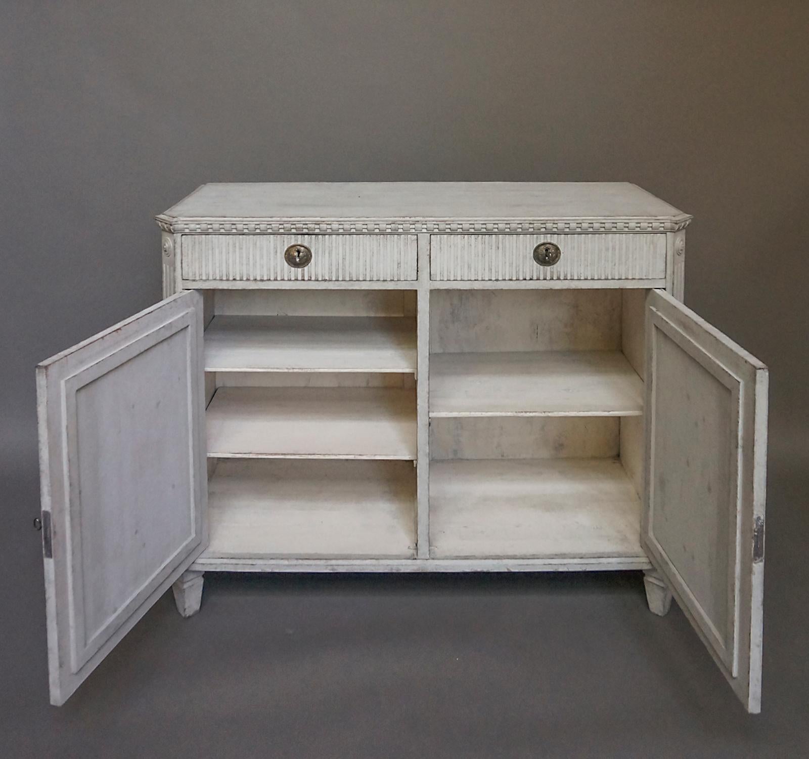 Two-door sideboard in the Gustavian style, Sweden circa 1880. Raised and reeded panels on the door with the same reeding on the two drawers above. Dentil molding around the top, canted corners and tapering square feet. The divided interior has two