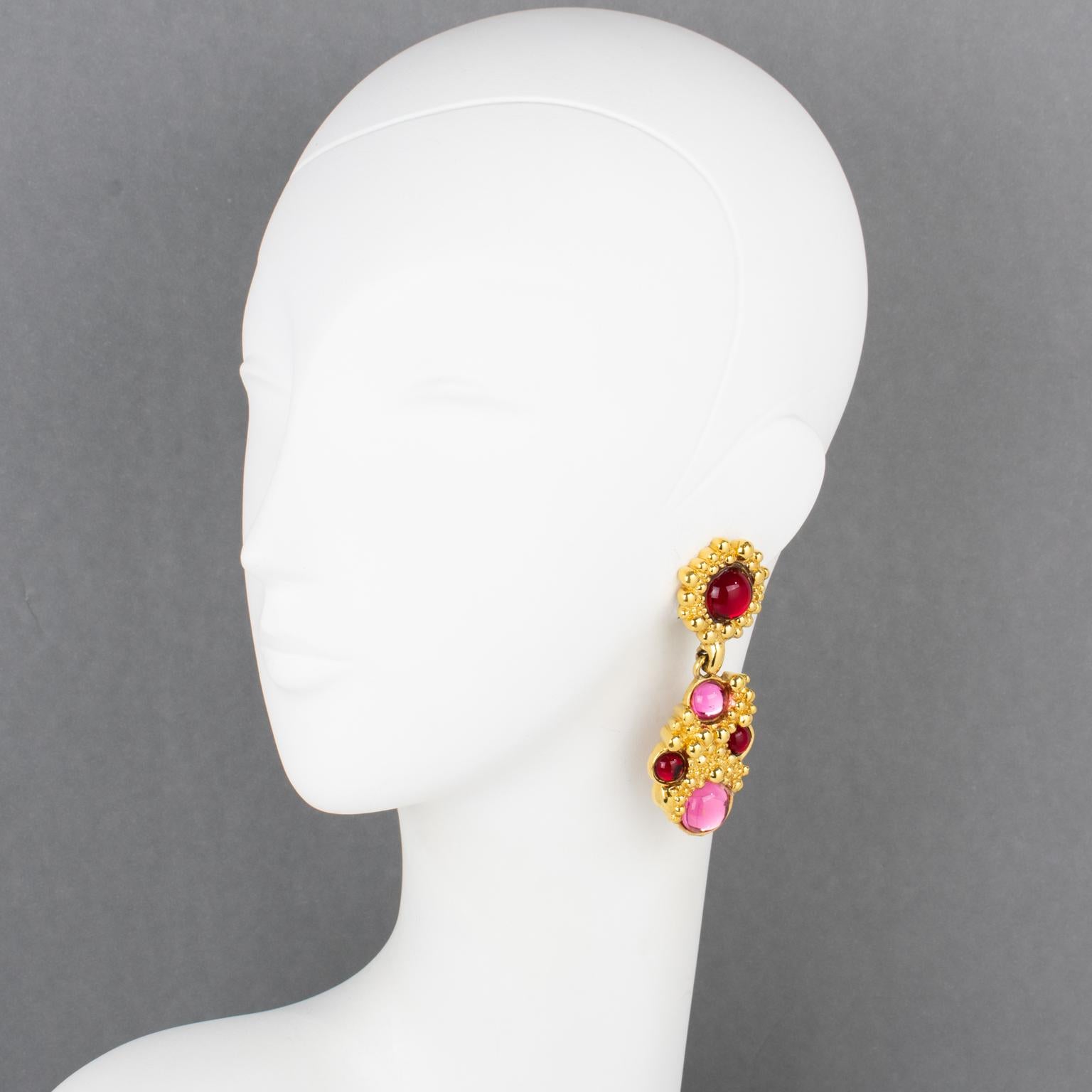 Guy Laroche Paris designed these elegant clip-on earrings. They feature a dangling shape with carved and textured gilded metal framing, ornate with ruby red and hot pink colored Gripoix poured glass cabochons. The Guy Laroche brand logo is engraved