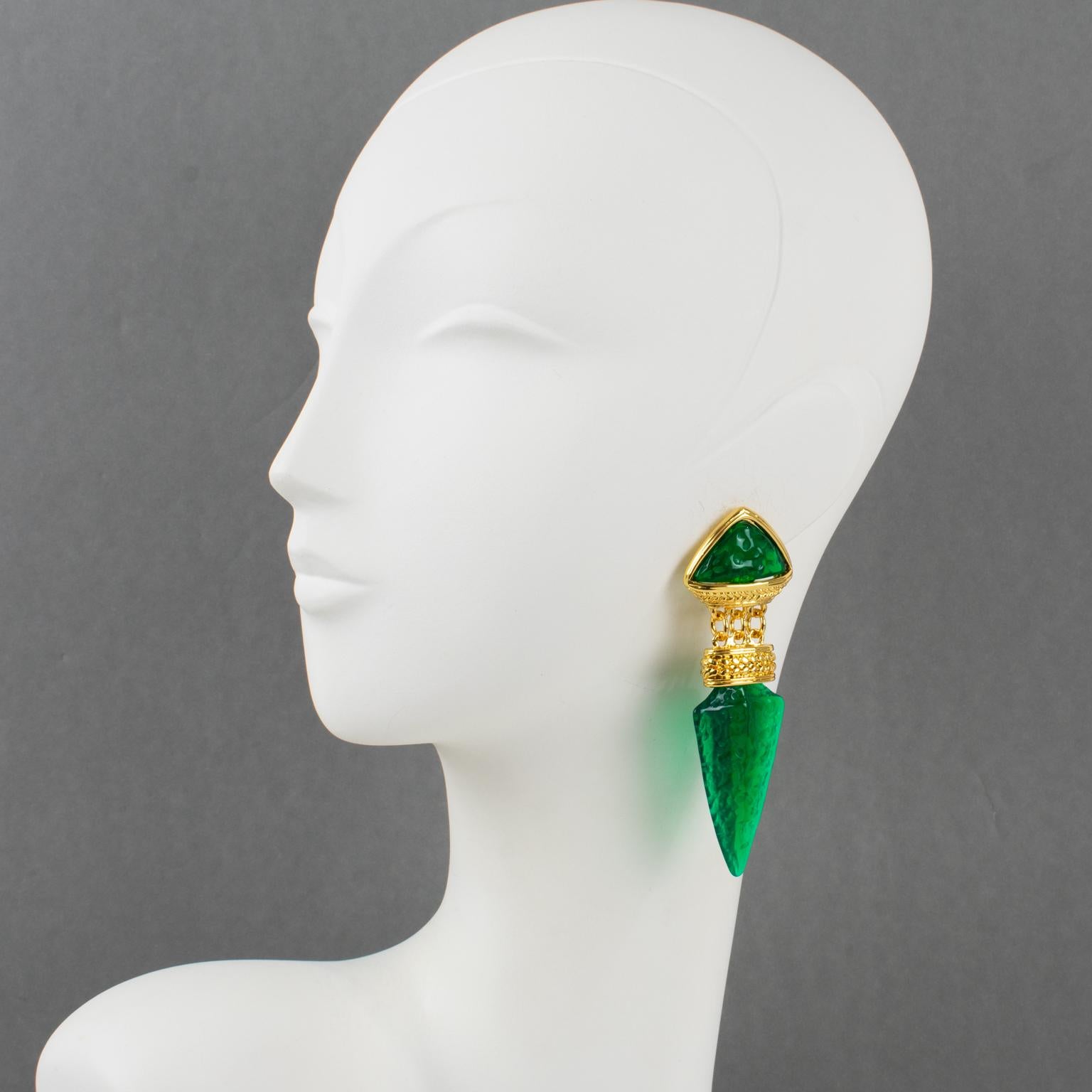 These elegant Guy Laroche Paris clip-on earrings feature a dangling shape with carved and textured gilt metal framing, ornate with emerald green resin carved cabochons and sword-tip-shaped beads. The engraved signature is at the back and reads Guy