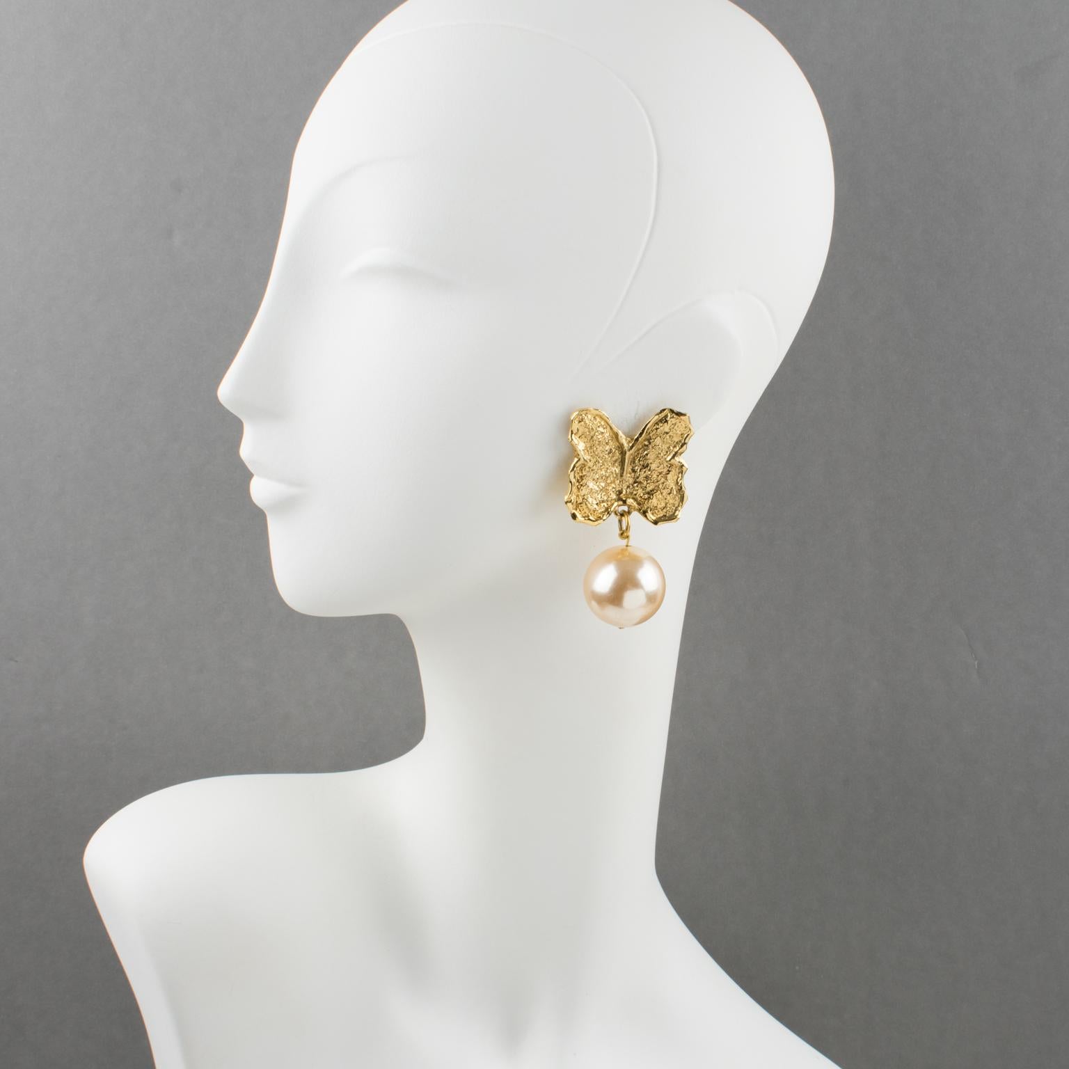 These elegant Guy Laroche Paris butterfly clip-on earrings feature an oversized, dangling shape with a carved and textured gilt metal butterfly, adorned with an impressive pearl imitation in a powder pink color. The engraved signature at the back
