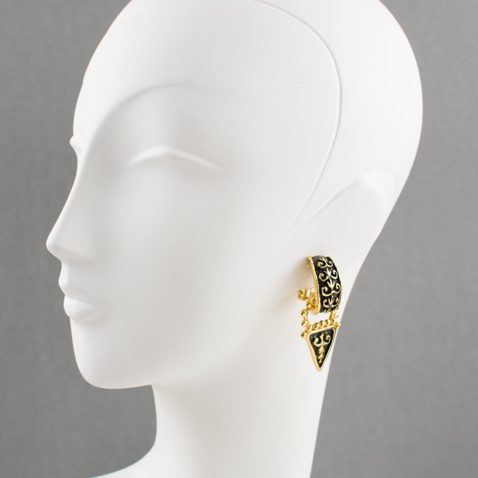 These elegant Guy Laroche Paris clip-on earrings feature a door knocker dangling shape with a Renaissance-inspired design in gilt metal all carved and textured, ornate with black enamel. The earrings have an engraved signature on the back reading