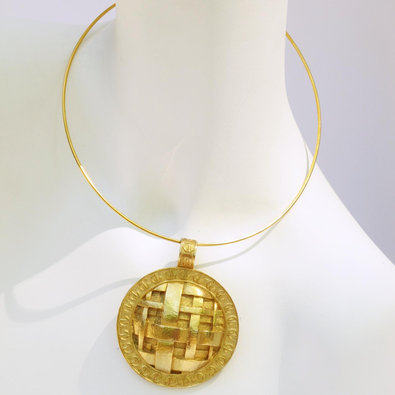 Questa imponente collana modernista firmata Guy Laroche Paris presenta un collare rigido in metallo dorato con un enorme medaglione dorato. Il medaglione in metallo è dimensionale con un design strutturato e un intaglio a treccia sormontato dal logo