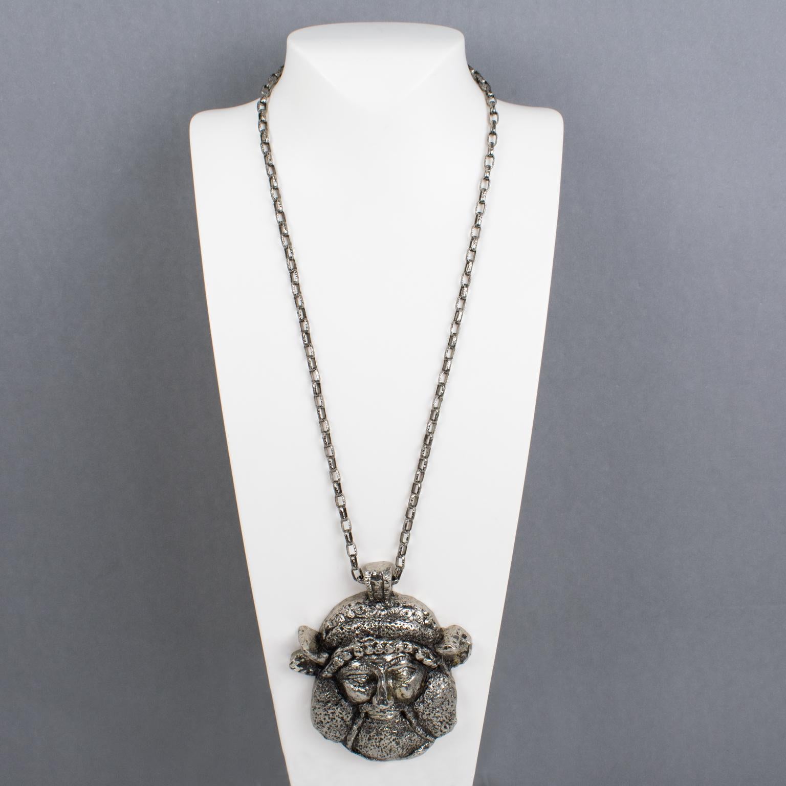 Questa splendida collana con ciondolo di Guy Laroche Paris rare è caratterizzata da una catena extra-lunga in metallo argentato con un ciondolo di grandi dimensioni. Il medaglione vanta un antico volto di dio vichingo in resina argentata rivestita