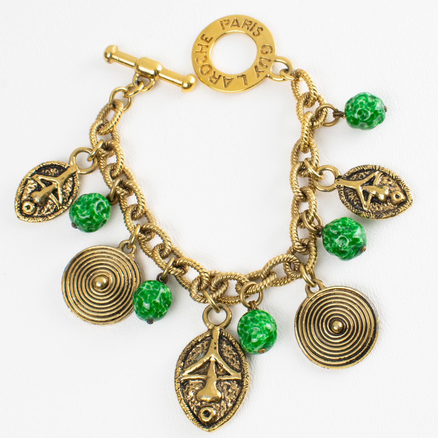 Questo raro bracciale a maglie tribali di Guy Laroche Paris presenta un design penzolante con charme a forma di maschera e scudo di ispirazione africana, forse di ispirazione Massai, con metallo dorato intagliato e strutturato, ornato da perline di