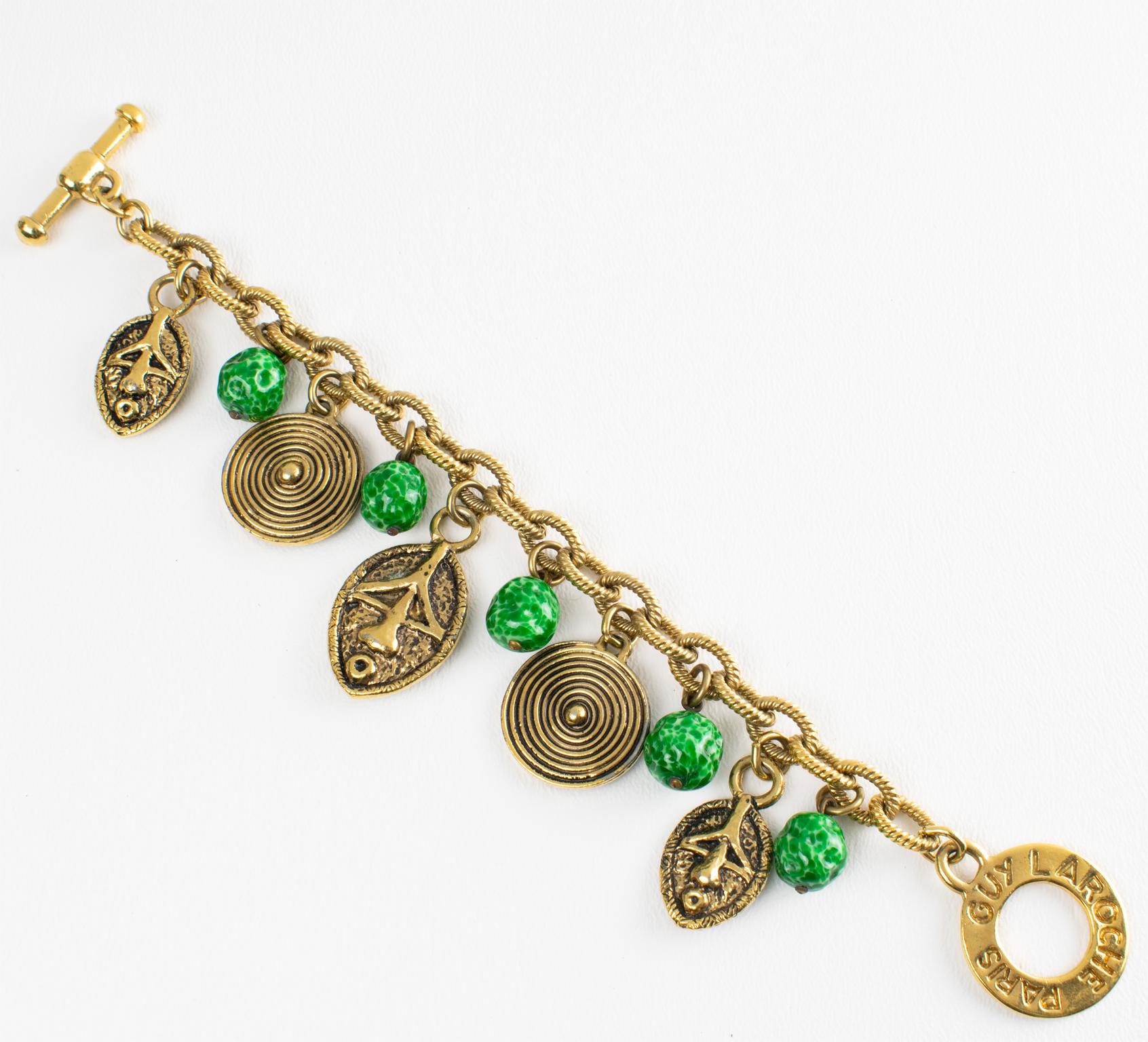 Ce rare bracelet à maillons tribaux de Guy Laroche Paris présente un design pendentif avec des charmes en forme de masques et de boucliers d'inspiration africaine, peut-être Massai, avec du métal doré sculpté et texturé, orné de perles de céramique