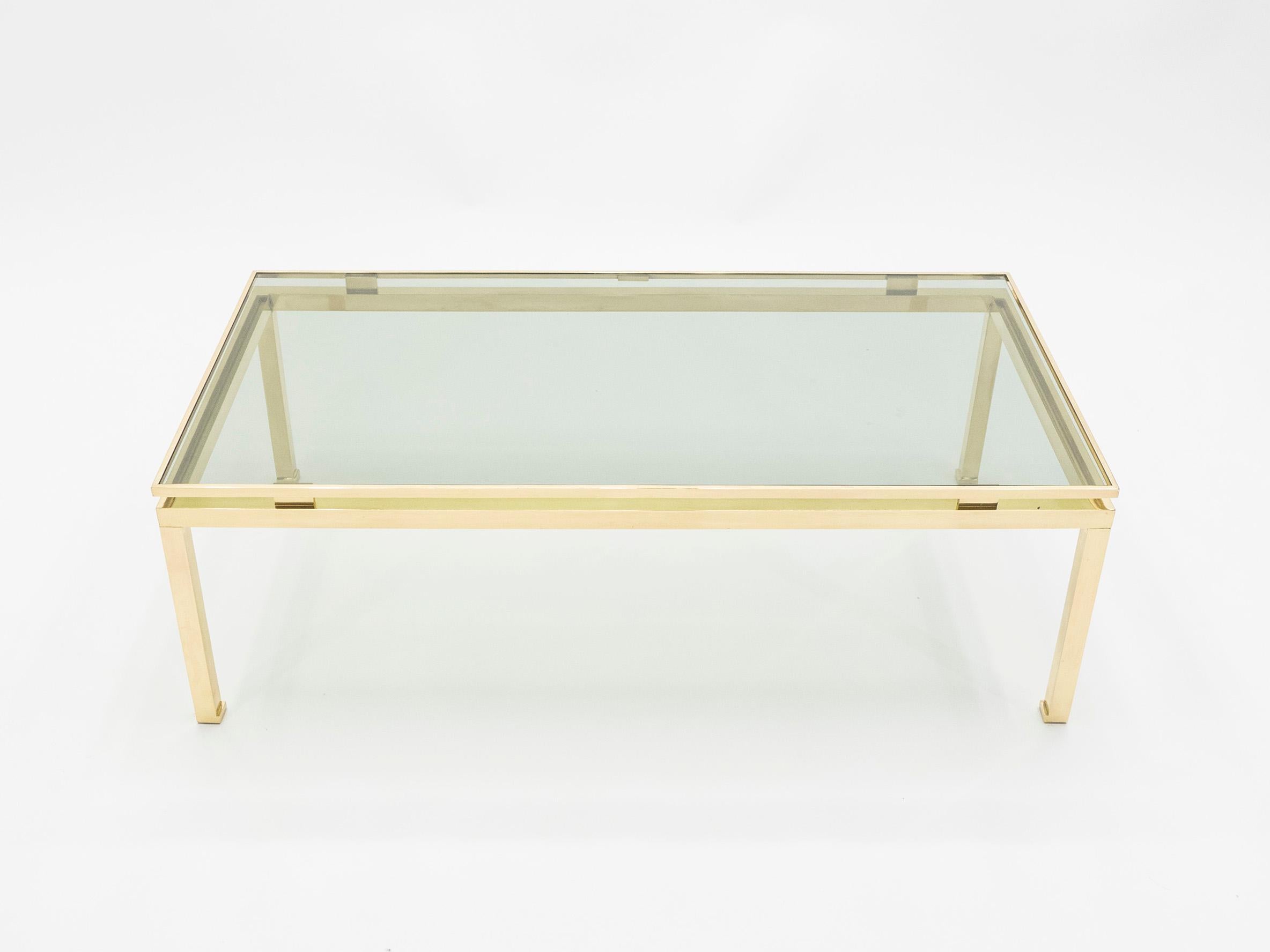 Simple lines and shiny point to this coffee table’s French Hollywood Regency roots. Designed by Guy Lefevre for Maison Jansen, it features shiny brass legs and a lightly smoked glass top. Its symmetry, elevated glass, and strong architectural design
