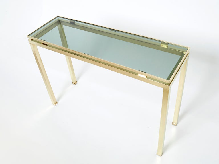 Minimalistic lines become lighter than air in this 1970s console table. Crafted by Guy Lefevre for Maison Jansen, it features sleek expanses of original green smoky glass set into a structured brass frame. Its symmetry, elevated glass, and strong