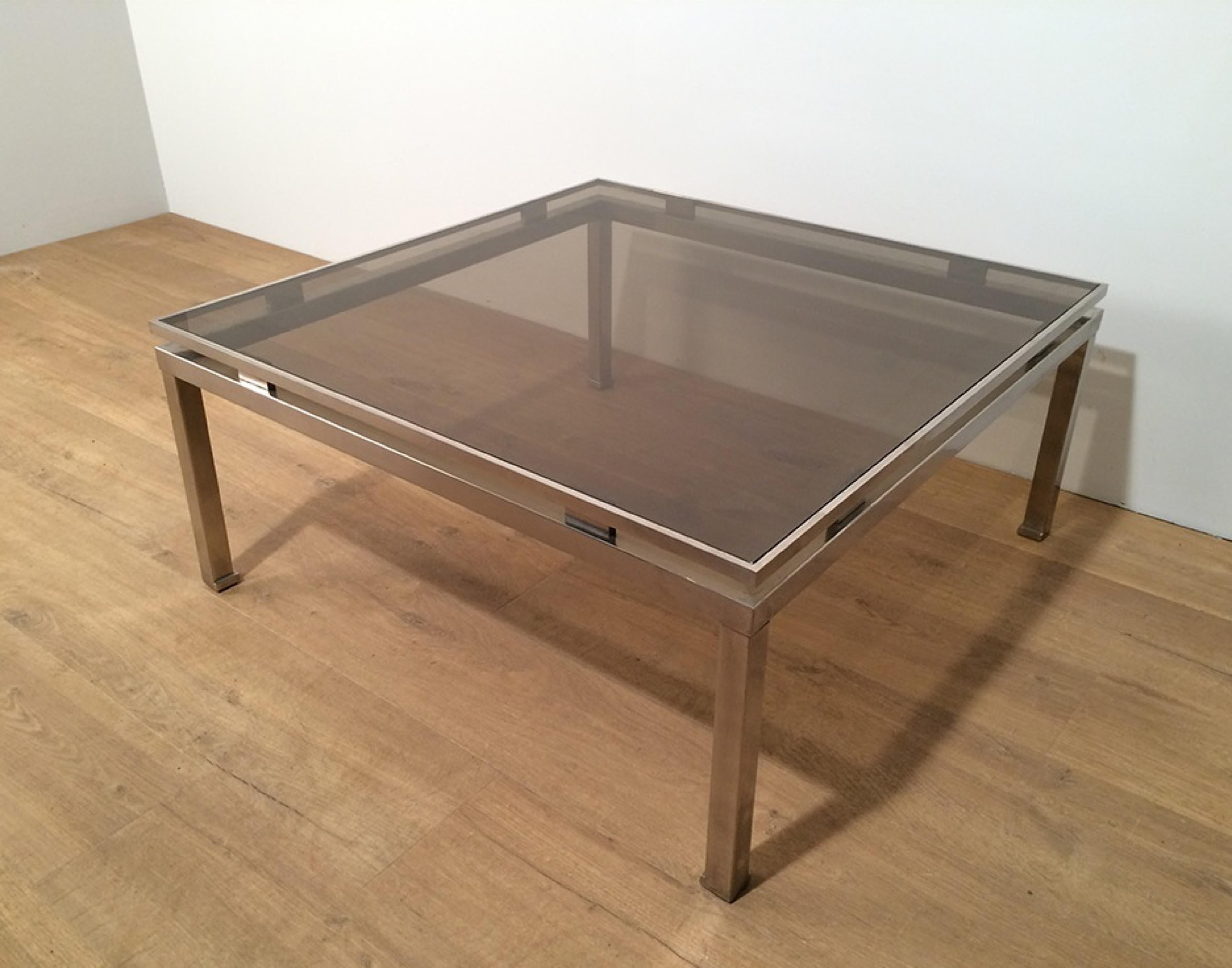 This nice square coffee table is made of brushed steel with a clear glass top shelf. This cocktail coffee table was made by famous French designer Guy Lefevre, circa 1970.