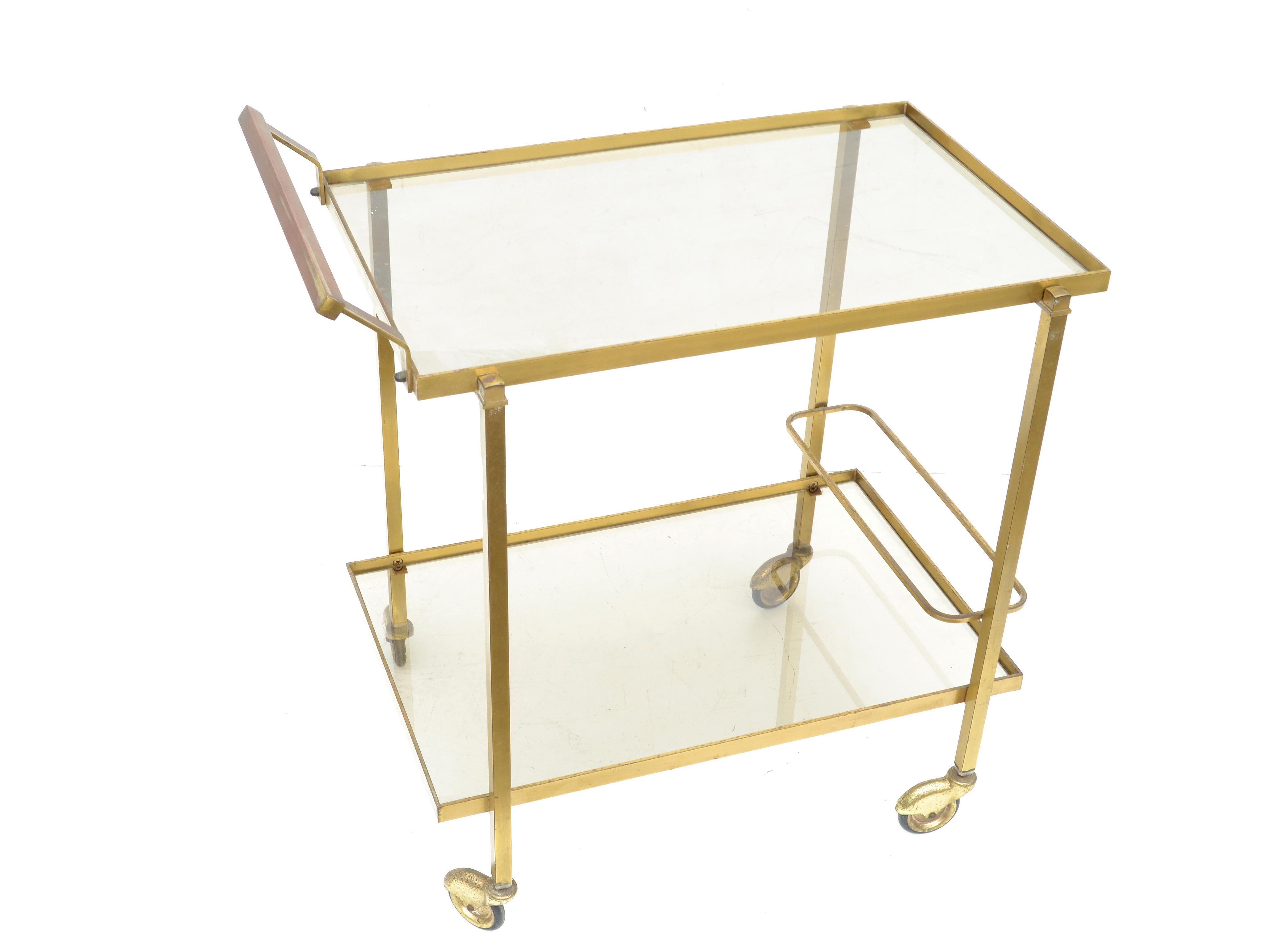 French Mid-Century Modern brass bar cart features two-tier glass shelves by Guy Lefevre for Maison Jansen. 
Made in the 1960 in patinated brass with smoked glass shelves and all original wheels.
Measures: 8 inches H from the floor to the 1st tier,