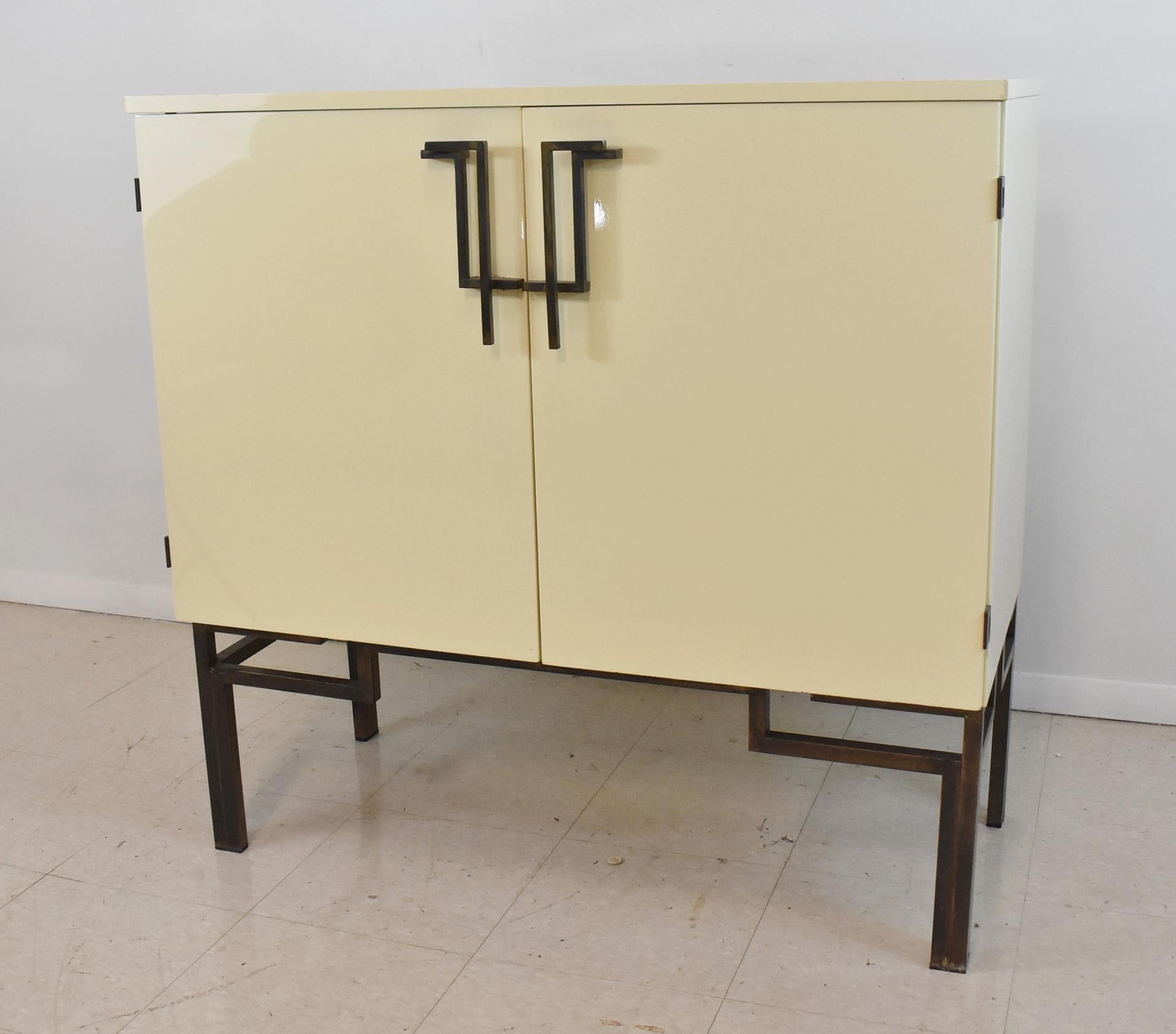 Mid-century modern 1970's bar cabinet by Guy Lefevre for Maison Jansen in a cream colored glossy lacquer with an Asian inspired frame and door pulls. The cabinet has 2 doors, an opening top, 1 drawer inside, and a mirrored interior. 40