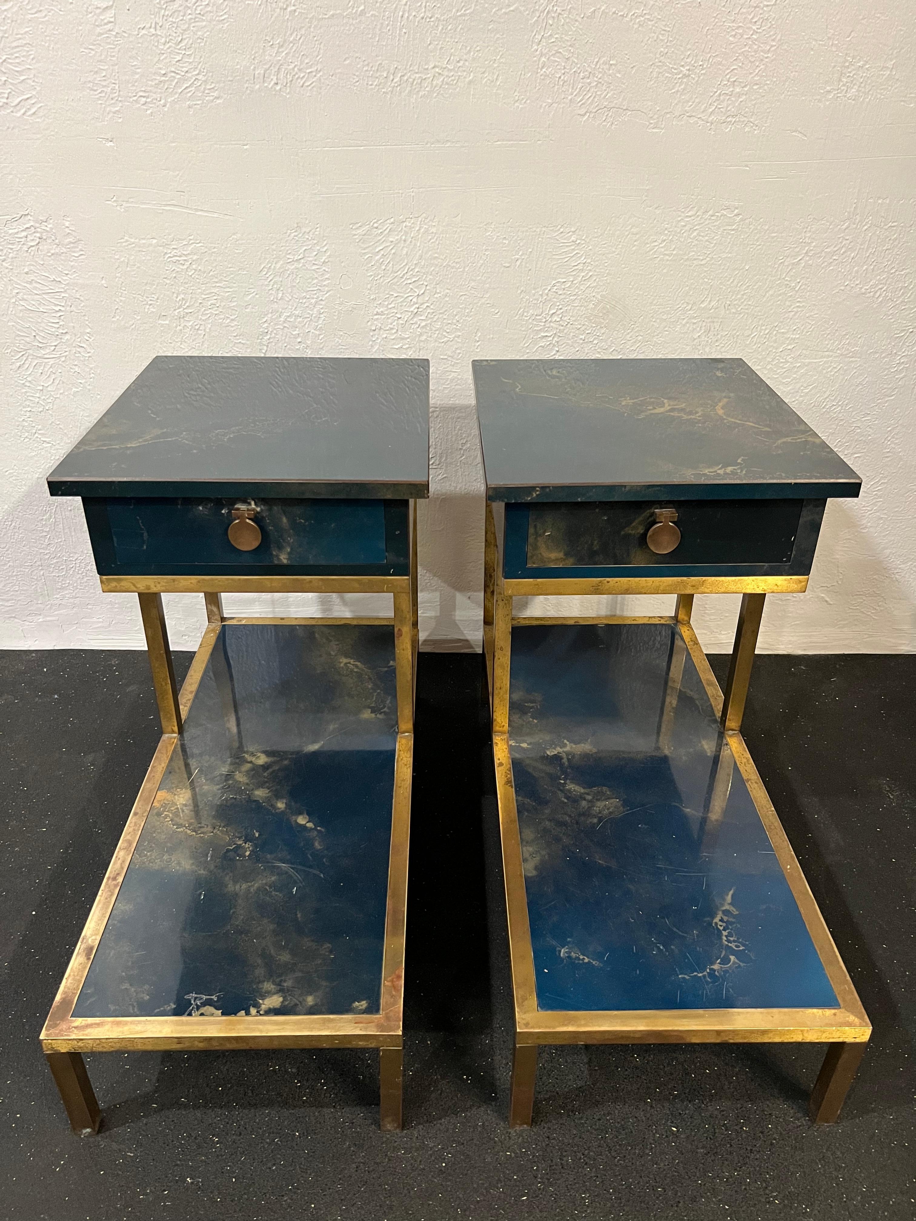 Pair of Guy Lefevre for Maison Jansen two-tiered lacquered and bronze tables. Rare examples that are unique to the market. Beautiful patina to the bronze found in the original state. Marbleized painted finish in blue and gold tones. Surface wear