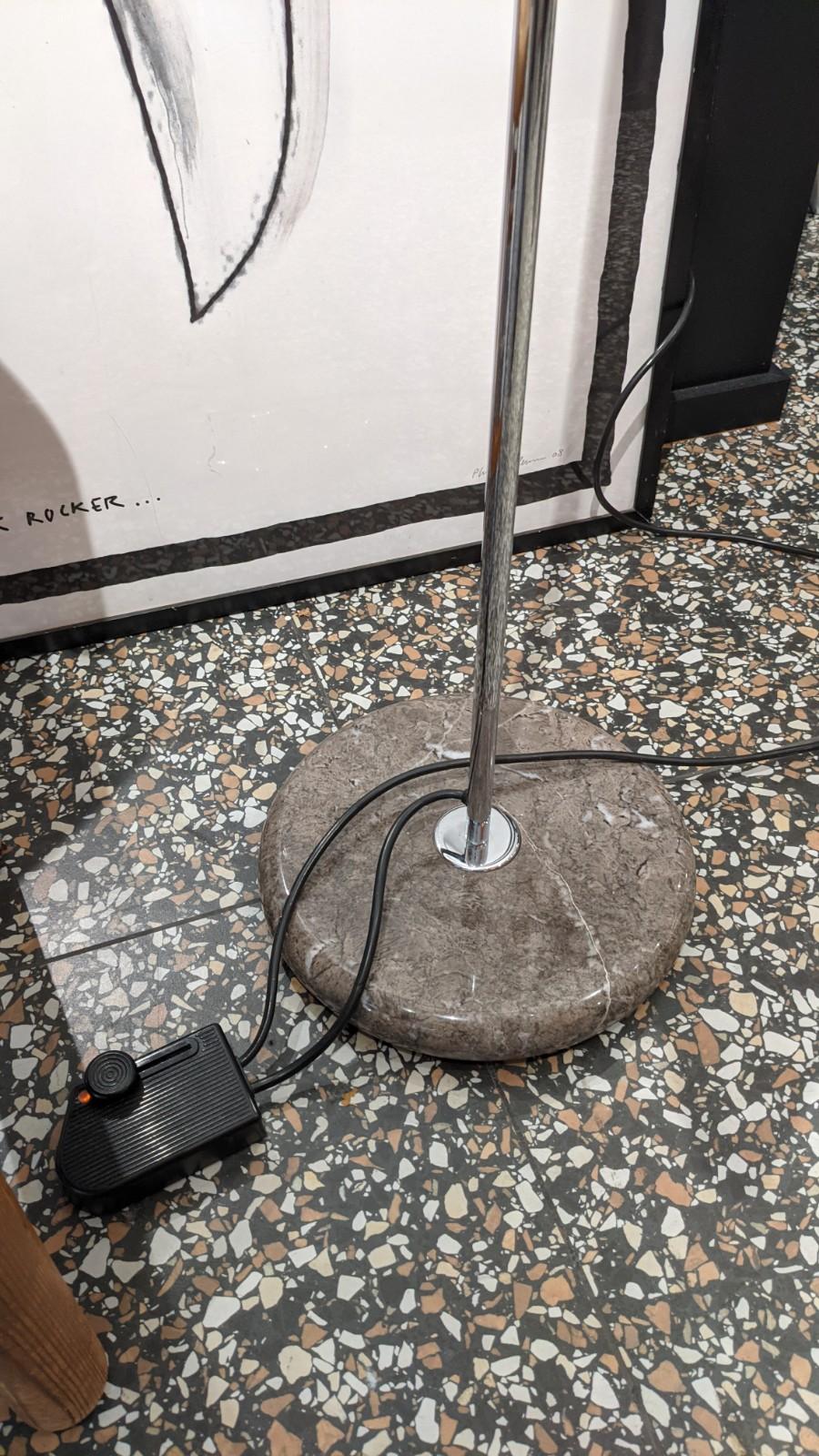 Floor lamp guzzini, brand visible on one of the pictures.
Rising and falling system and adjustable. 
Mondragone marble foot, stainless steel tube and plastic white and black lamp.

This floor lamp is very bright for the private area and for the