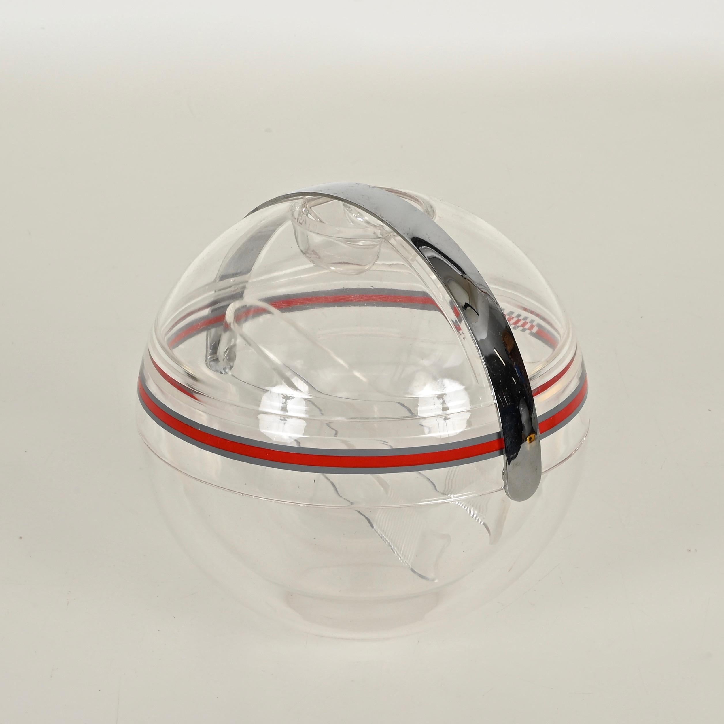 Magnifique seau à glace en plastique transparent en forme de boule, édition limitée du milieu du siècle, avec sa pince à glace d'origine. Cette pièce fantastique a été conçue par Guzzini à Recanati, en Italie, dans les années 1970.

Cet étonnant