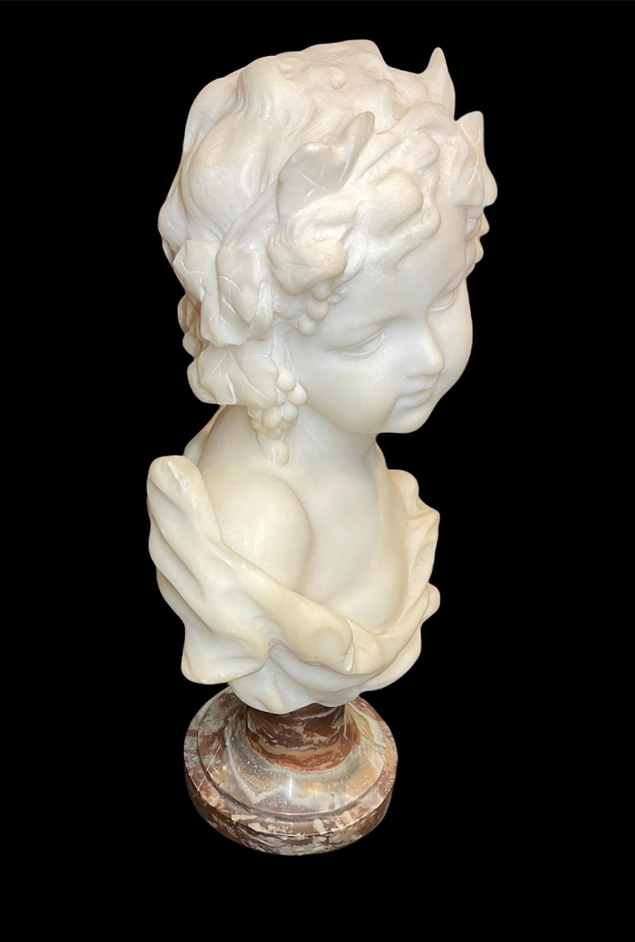 This a white marble bust of the Allegory of Autumn. It is depicting a young girl with a very expressive eyes. Her chest Is covered by a robe and her curly hair adorned by leaves and branches of grapes. The bust is attached to a brown round marble