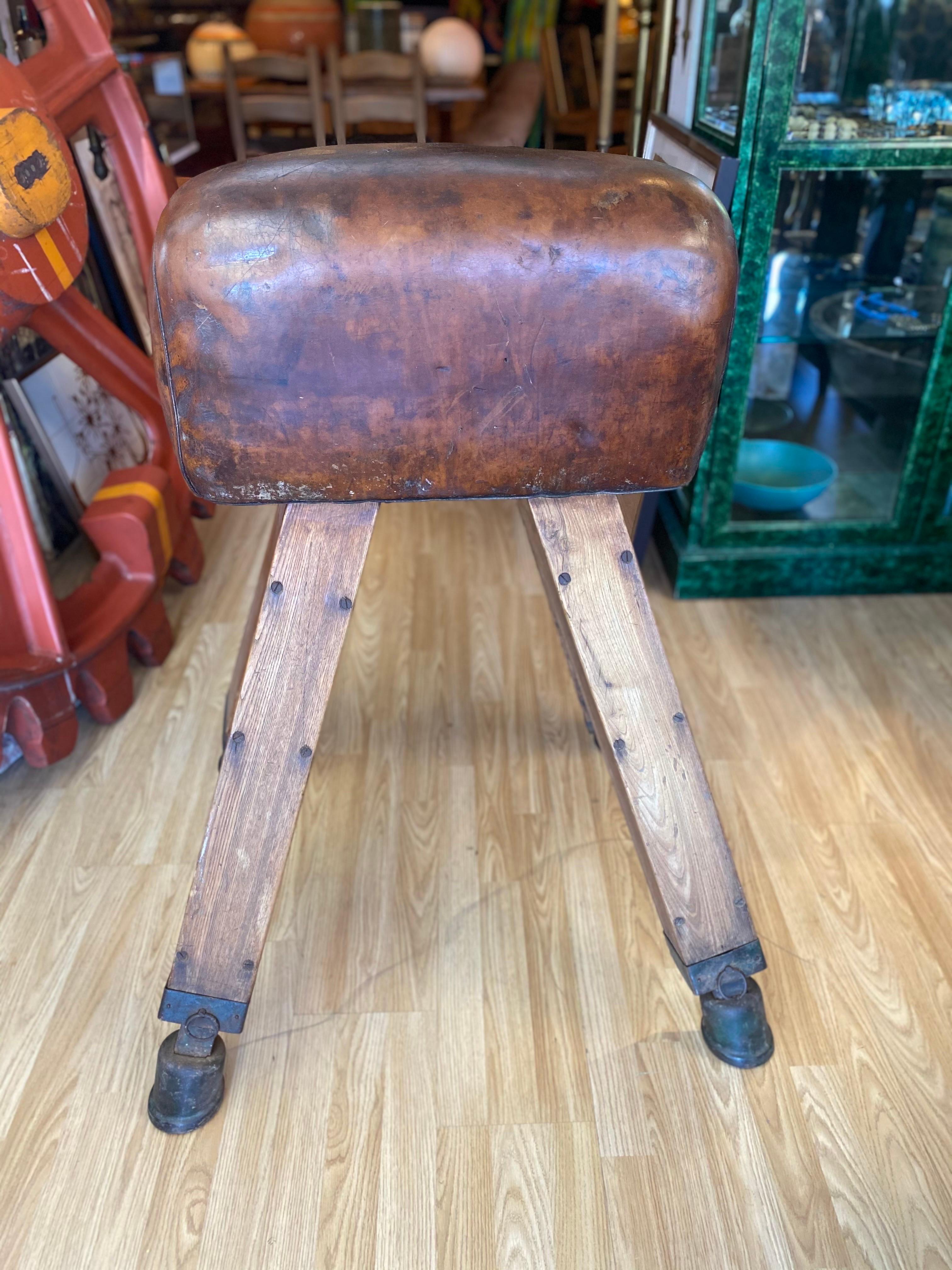 Beautiful early mid-century gymnastic pommel horse/bench vault. Features an oak and iron frame covered with a patinated deep cognac colored leather and a few deep scratches in leather as shown in images. This piece is very heavy and solid with