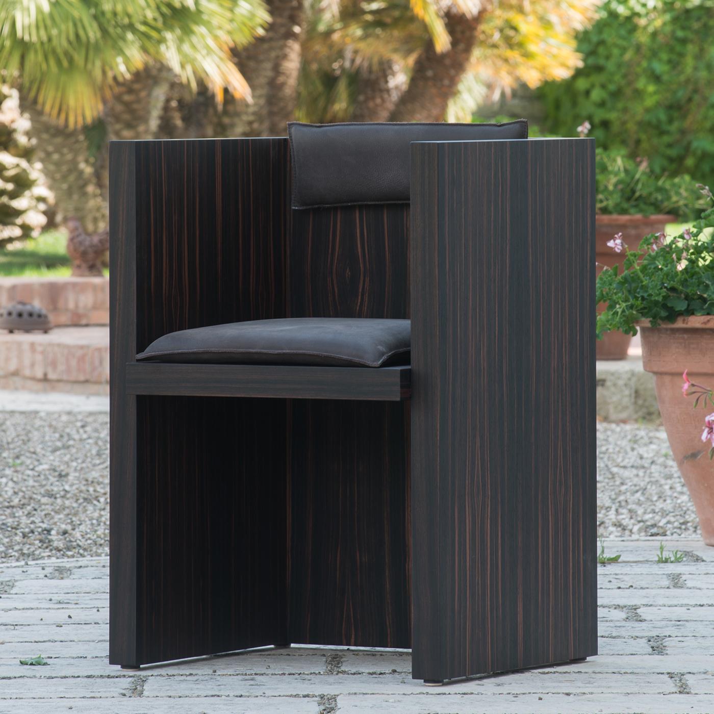 This boxy, square chair is shaped in the form of an H. Made from ebony wood that originated in Madagascar, it has a regal, authoritative, throne-like look, making it perfect for a home or office setting. Its dark structure is accented by genuine