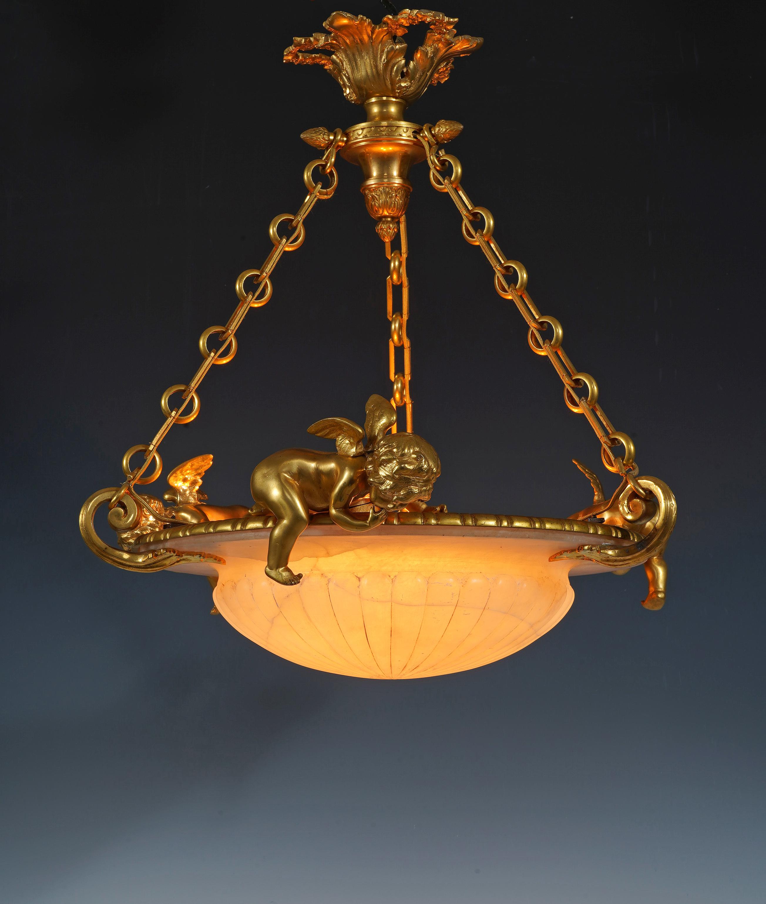 Affascinante lampadario in stile Luigi XVI composto da un bacino scolpito in alabastro circondato da un fregio in bronzo cesellato e dorato su cui si trovano tre piccoli Cupidi alati che guardano verso il basso.
Il tutto è sospeso a un'elegante