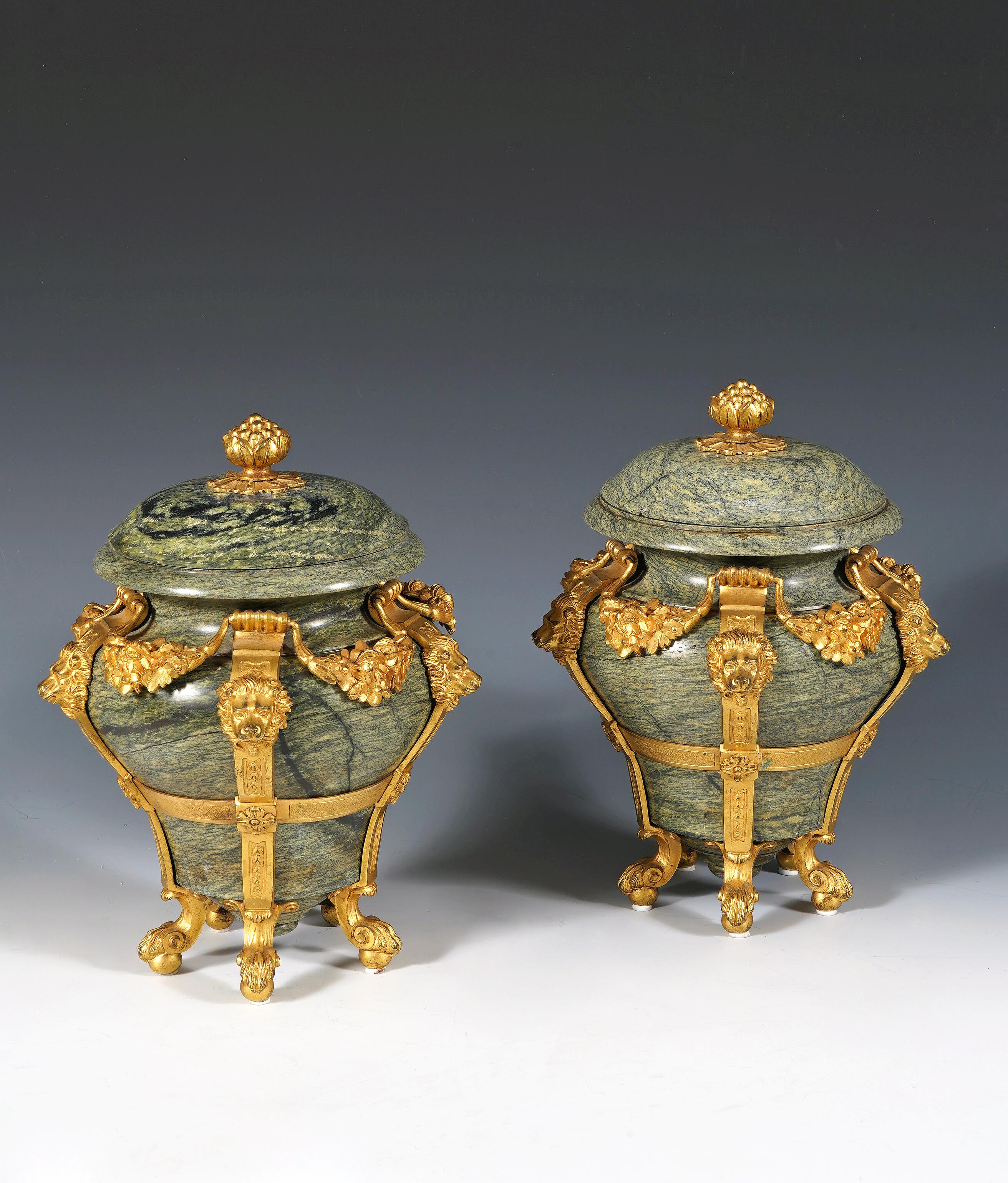 Beautiful pair of green marble covered vases, set in an elegant chiseled and gilded bronze mount, decorated with lion heads alternating with garlands of flowers. The molded lid is topped with a finial in the shape of a grenade. They rest on five