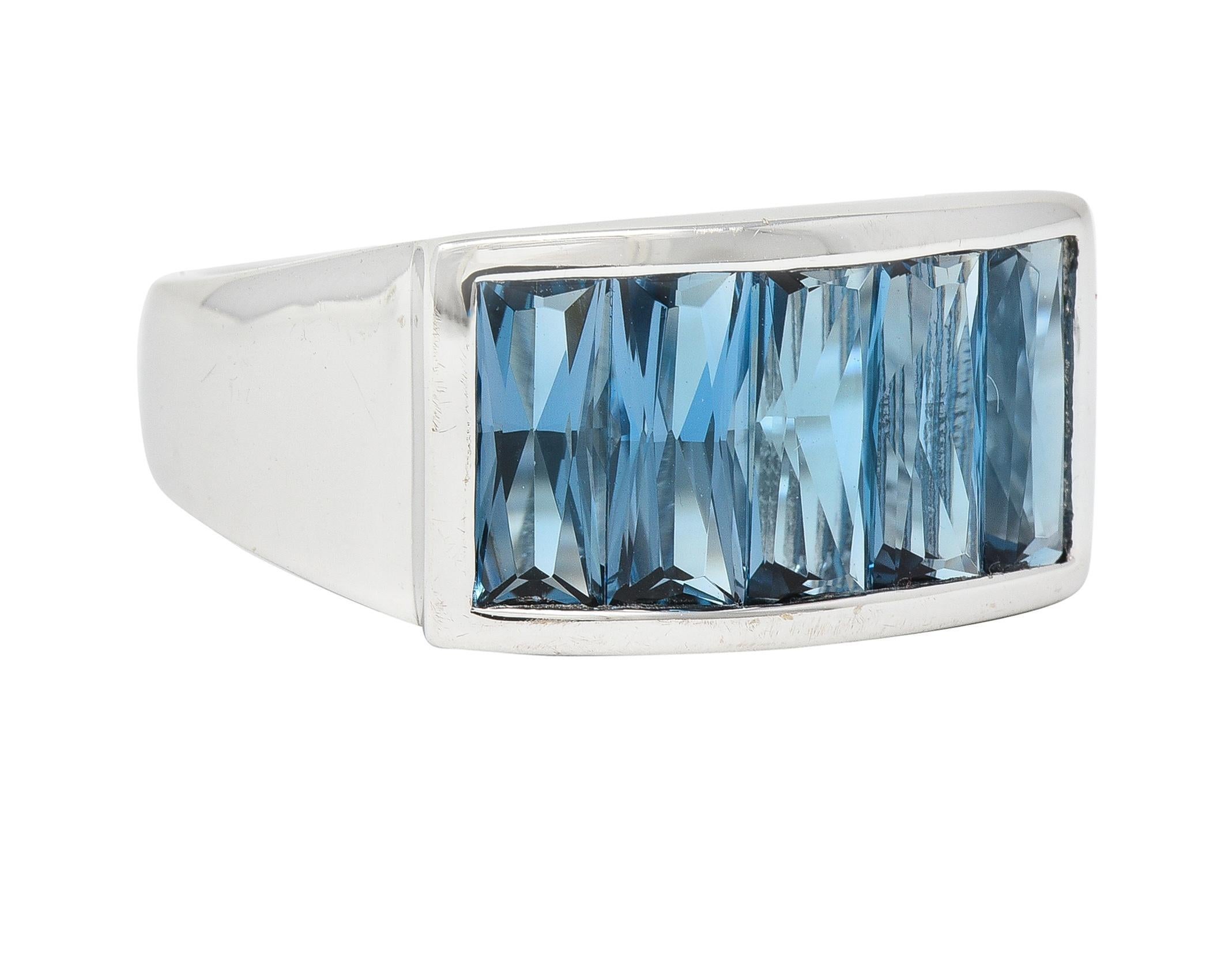 Centering five French cut topaz weighing approximately 5.00 carats total
Transparent bright blue in color with light saturation
Set east to west in a raised channel
With high polish surround 
Stamped for 18 karat gold
With maker's mark for H.