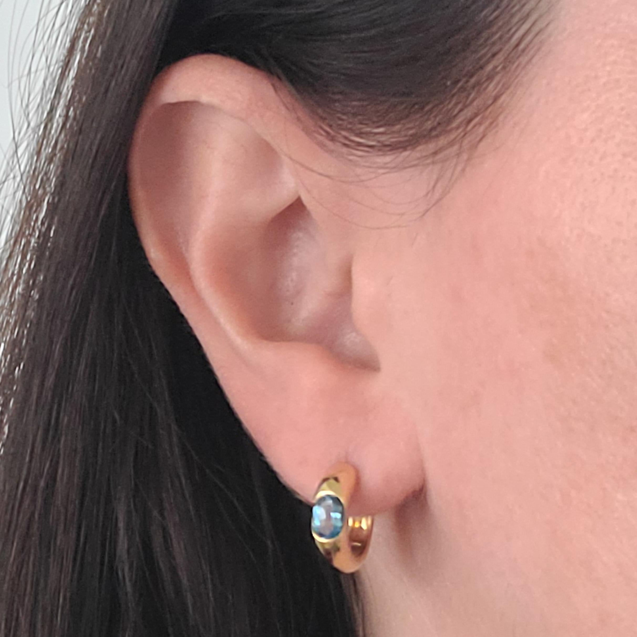 H. Stern 18 Karat Yellow Gold 4.55mm Wide Rounded Huggie Hoop Earrings Featuring 2 Oval Cut Blue Topaz. 15mm Diameter. Pierced Post With Hinge Closure. Finished Weight Is 4.8 Grams.
