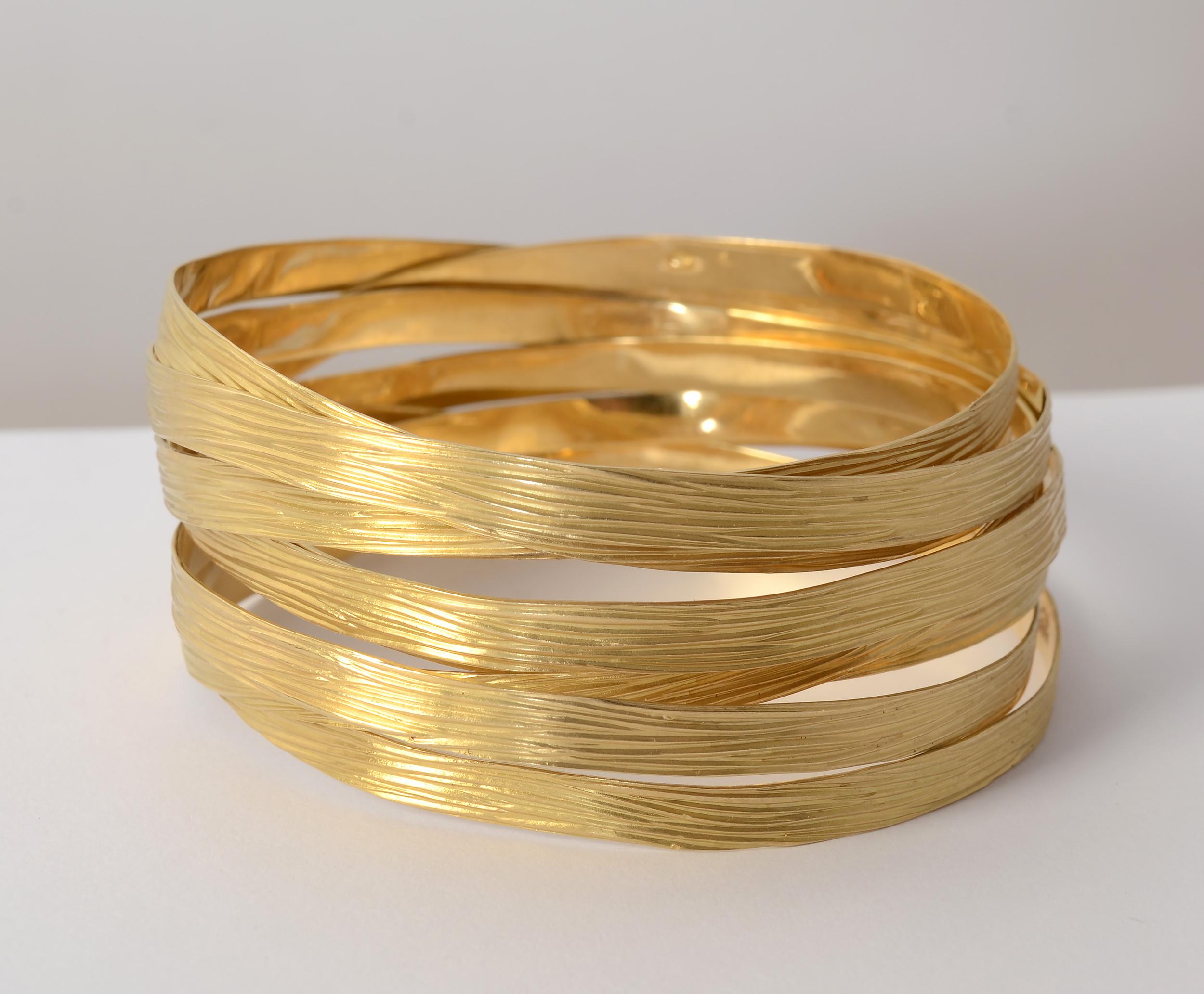 Eight interlooped bangle bracelets make a stunning sculptural statement. The flat gold bands are enhanced with a striated texture. Each bangle is 3/8