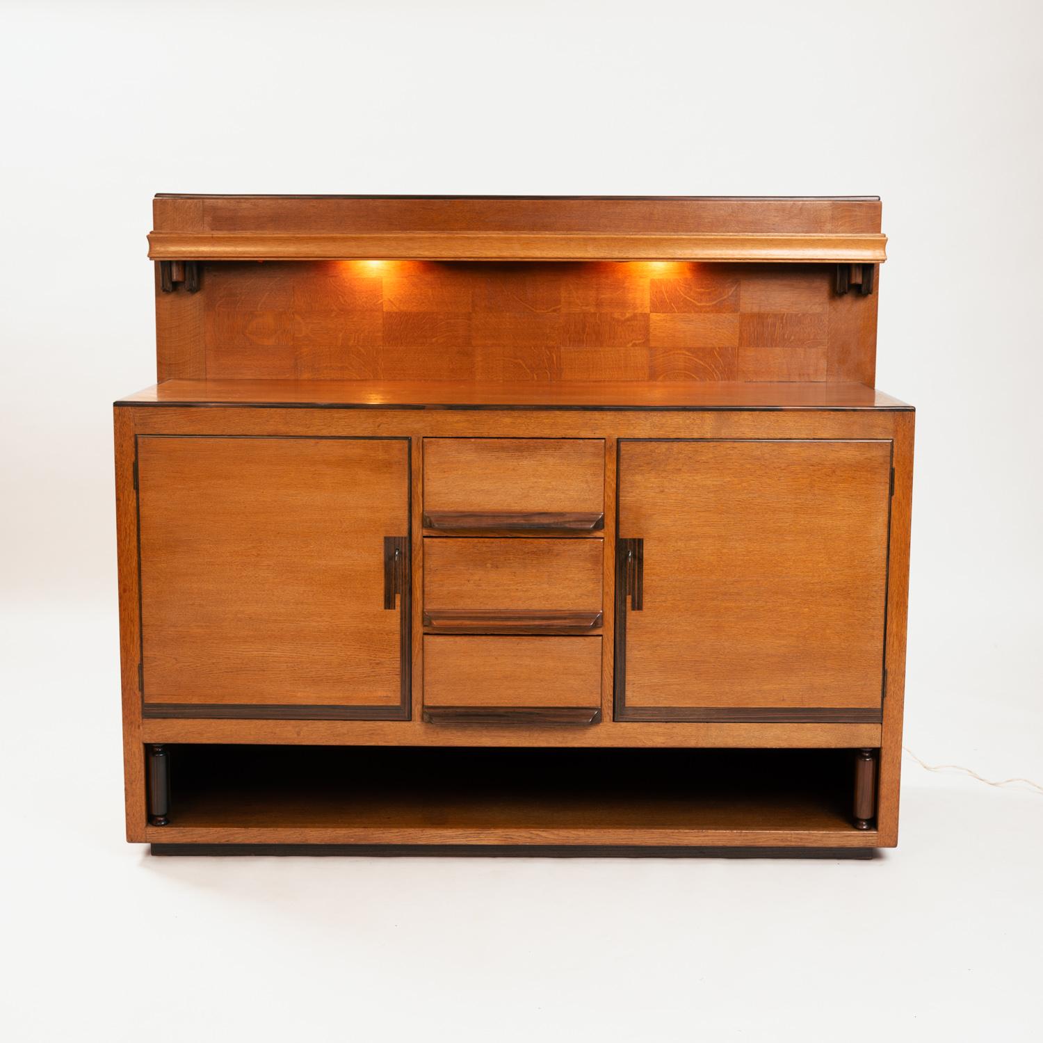 This beautiful art deco sideboard is a rare example of Haagse school design by designer and Carpenter Anton Lukas in the early 1930s.
The sideboard is made of oak and macassar ebony wood. 
Under the top shelves, there is the original lighting, but