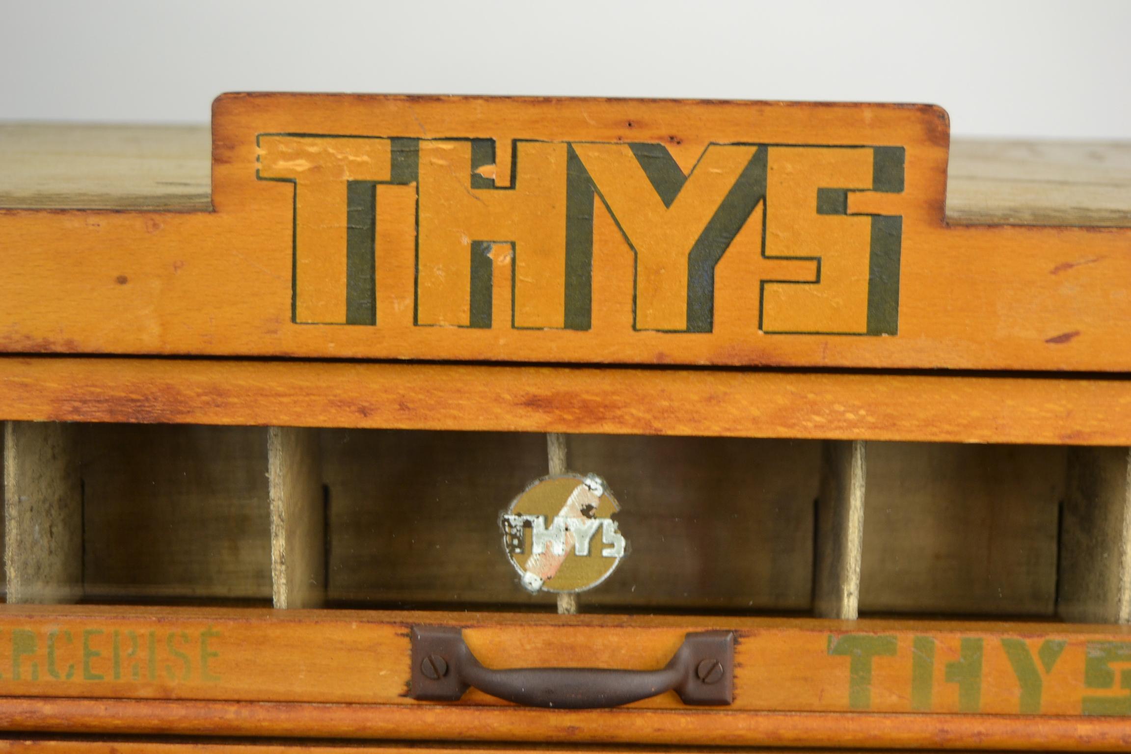 Vintage-Kurzwaren-Werbeschrank für Nähgarn der Marke Thys Belgium. 
Dieser Aufbewahrungsschrank für Nähmaterial hat 4 Schubladen mit den originalen Metallgriffen. 
In den Schubladen ist teilweise eine hölzerne Trennwand vorhanden - ein Glas wurde