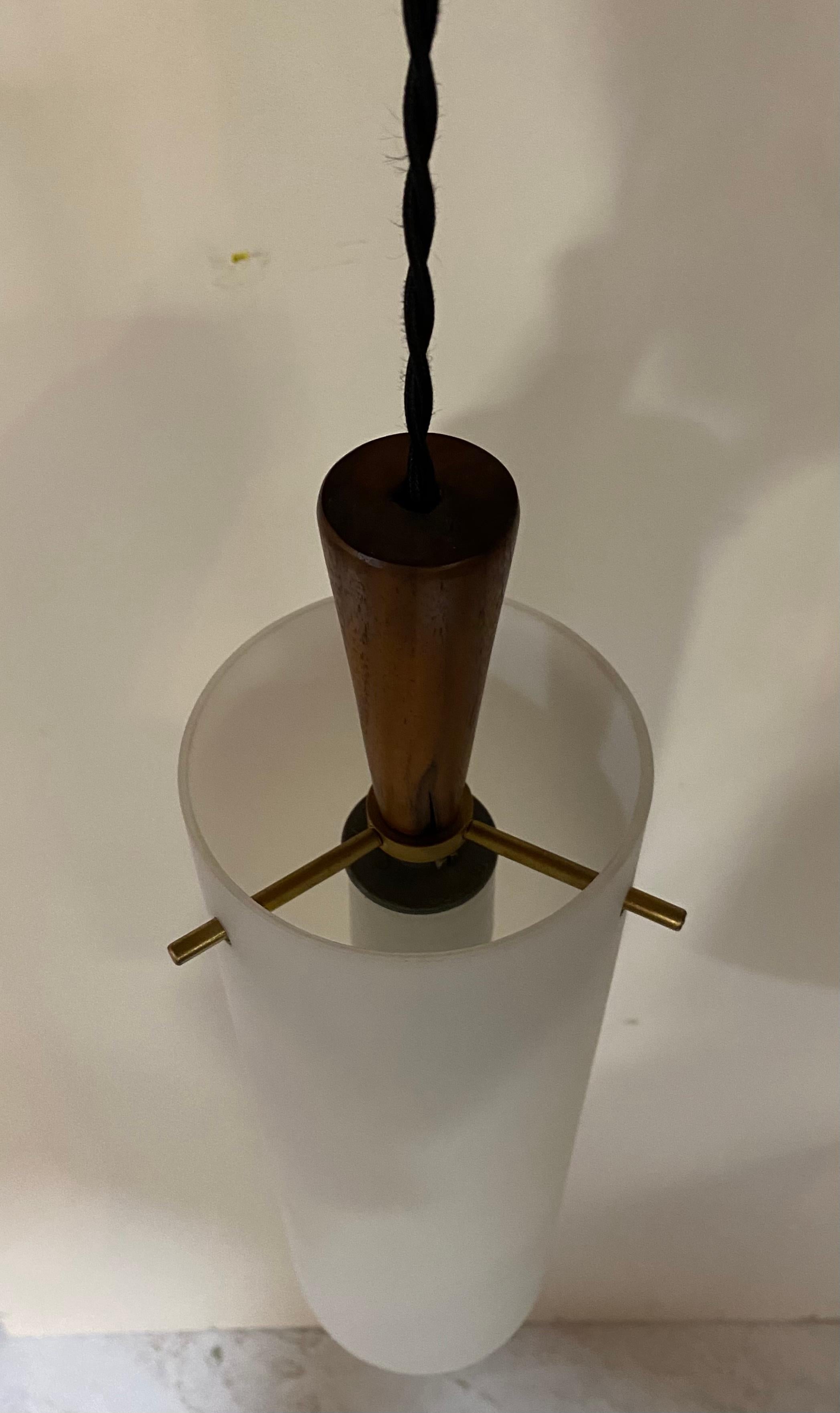A light fixture by Hadeland Glasswverk of Norway, featuring a frosted glass cylindrical shade complemented by brass pin holders and walnut cap, circa 1950.

Unsigned but widely documented. Takes one standard US bulb, 60 watts max.

Dimensions: 4