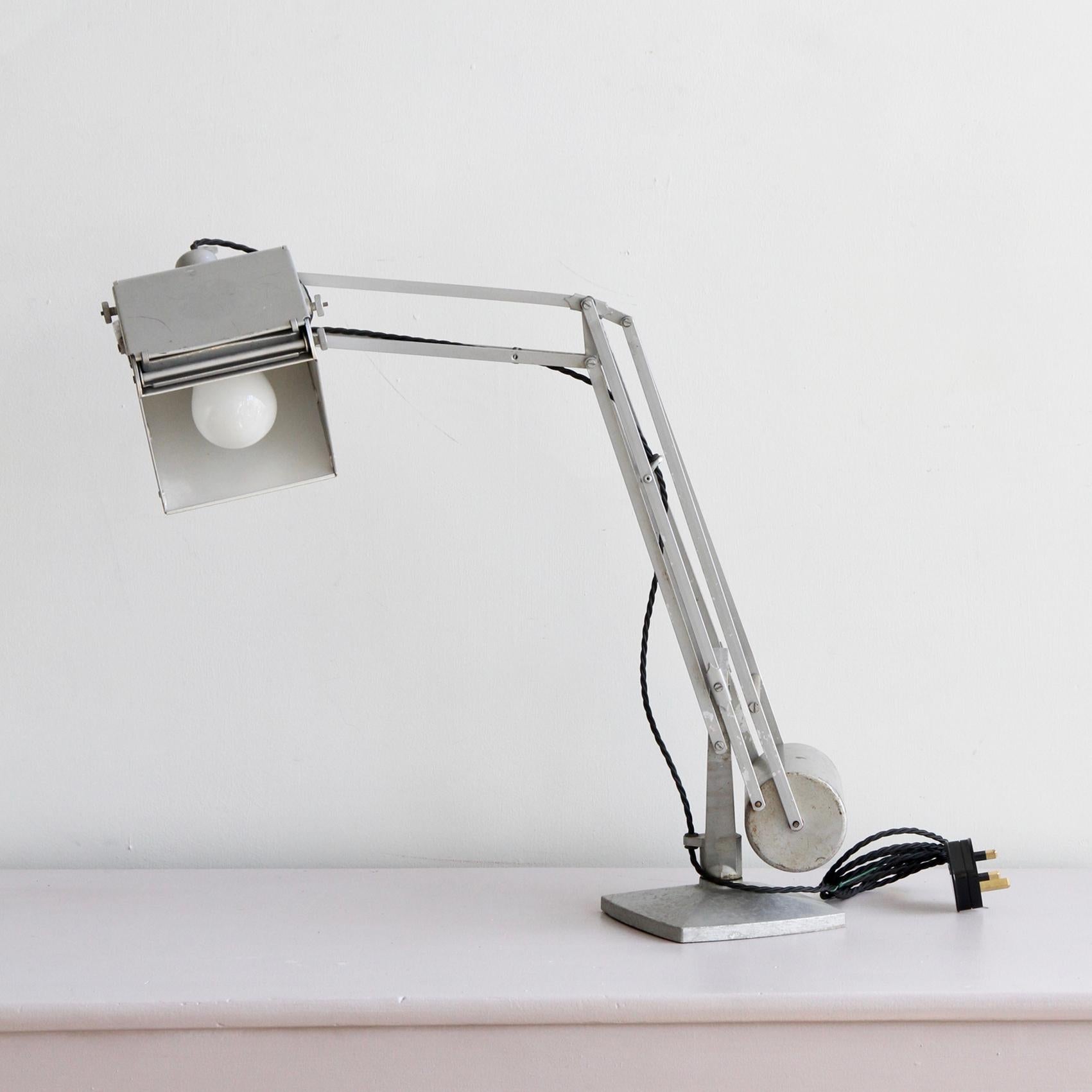 A Hadrill and Horstmann “Pluslite” desk lamp circa 1940s. The silver grey adjustable frame with counter balance features the cast H & H monogram and a retractable magnifier. The unique design of the steel counterbalance, which rolls in full motion