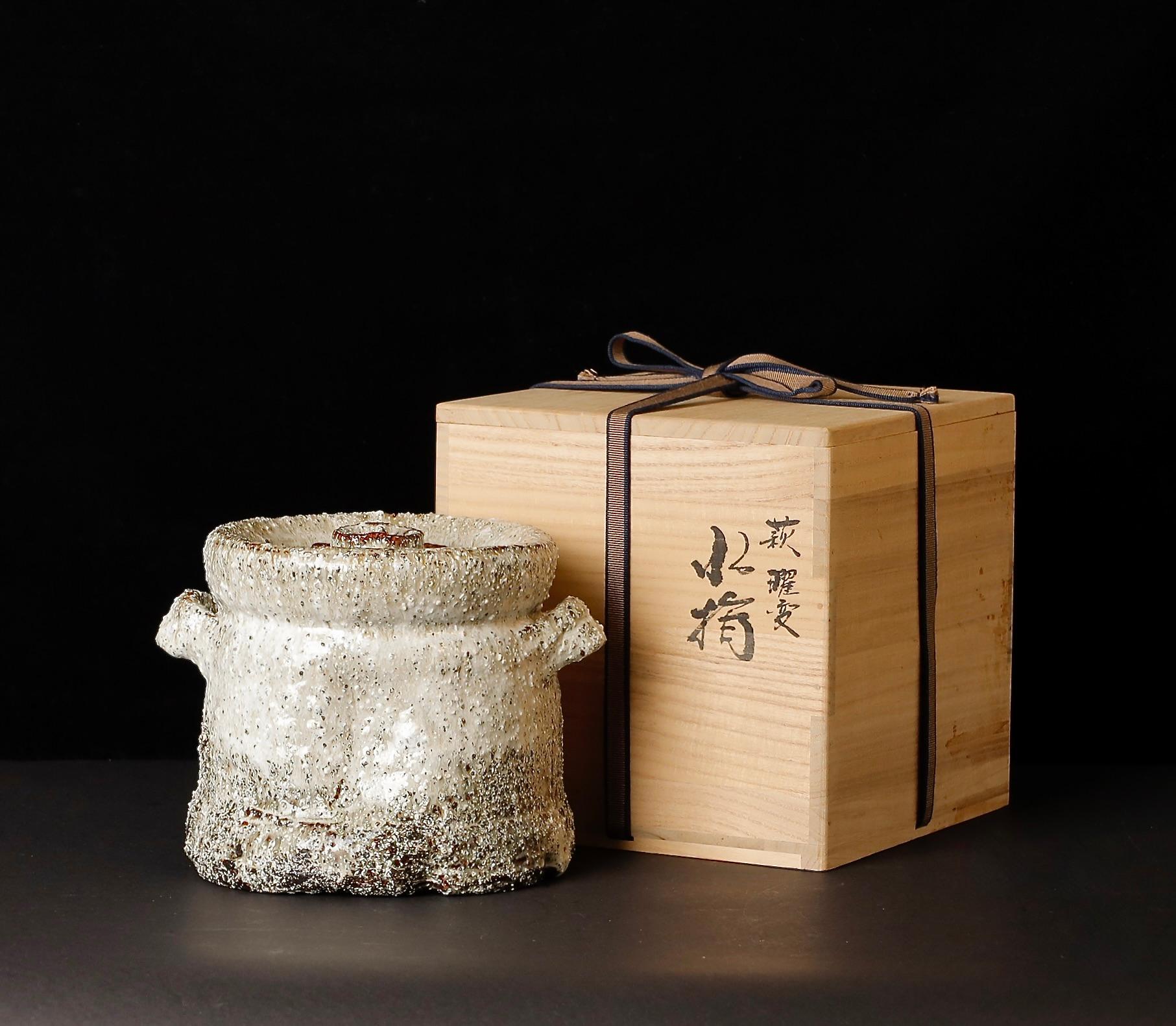 Un precioso mizusashi (recipiente de agua cubierto) hecho a mano por el célebre ceramista de Hagi Mashita Takashi (nacido en 1952), que ejemplifica la estética cálida y táctil y el tranquilo refinamiento por los que se conoce a Hagi-yaki. La vasija