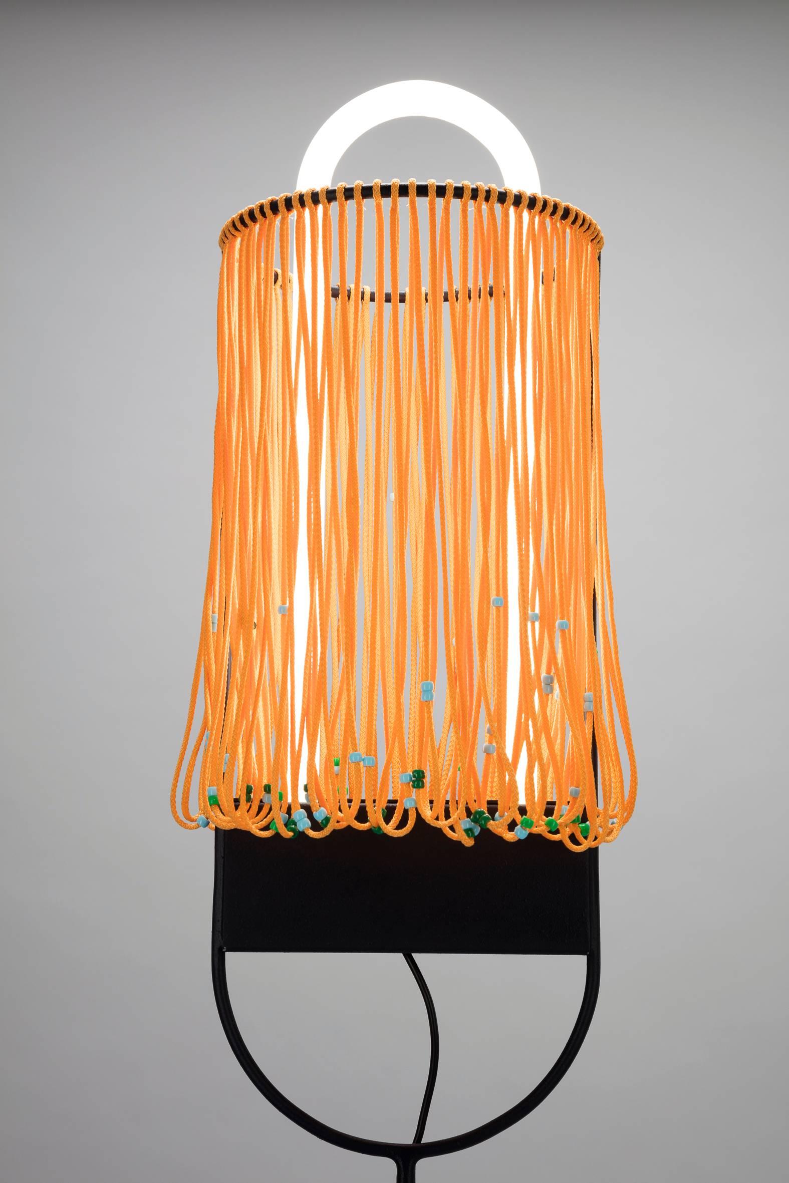 A collection of colorful standing lights with a curved neon light erecting through a ring of hanging ropes, with plastic pearls. 

Designer: Clemence Seilles 
Materials: Neon light, metal, rope
Dimensions: 27 x 156 cm
Weight: 5.716 kg.