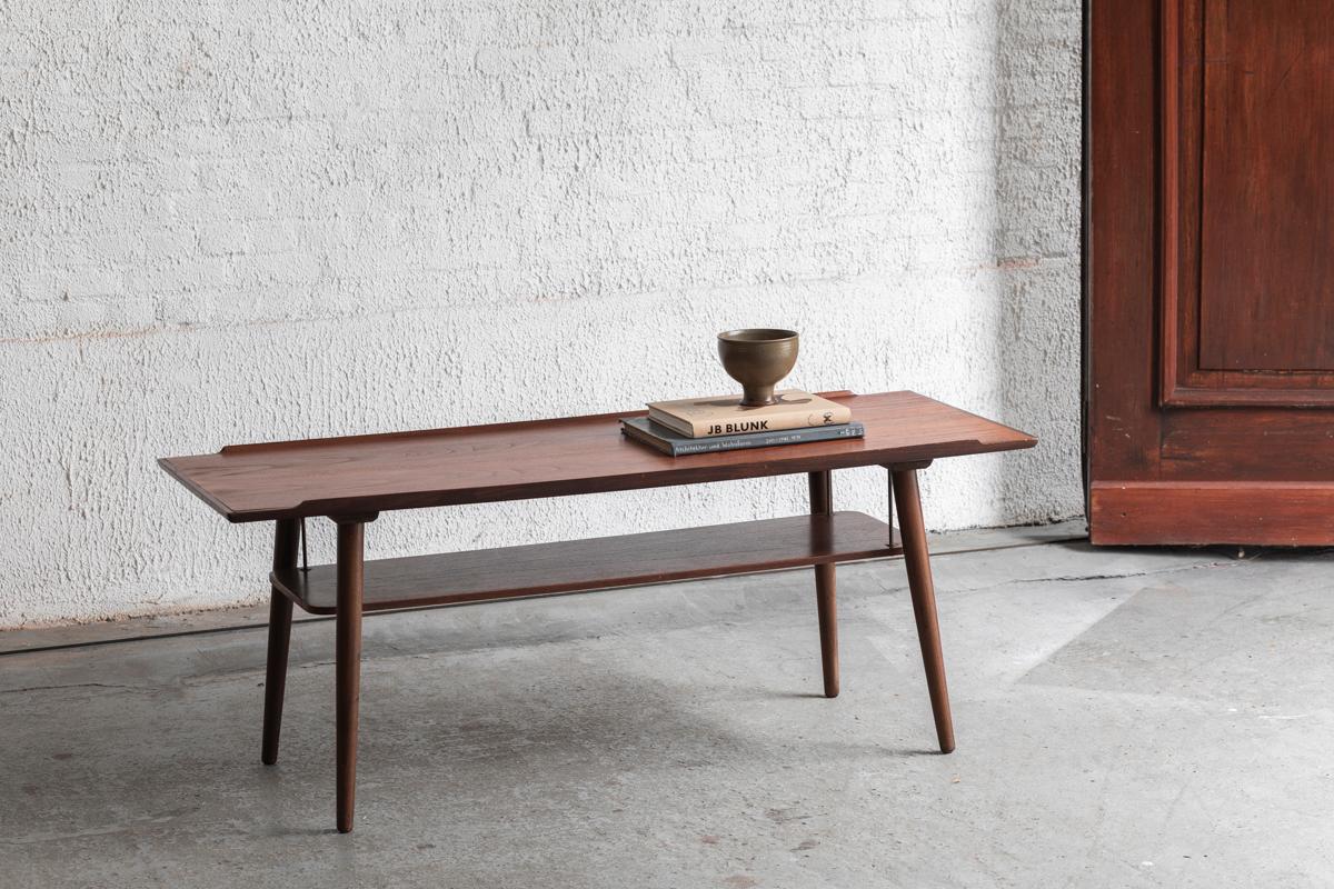 Coffee table designed by Hakon Madsen and produced in Aarhus, Denmark around 1960. Solid teak wooden frame and  a teak veneered top and magazine holder were combined with messing details. In very good condition. Parts of maker’s label still visible