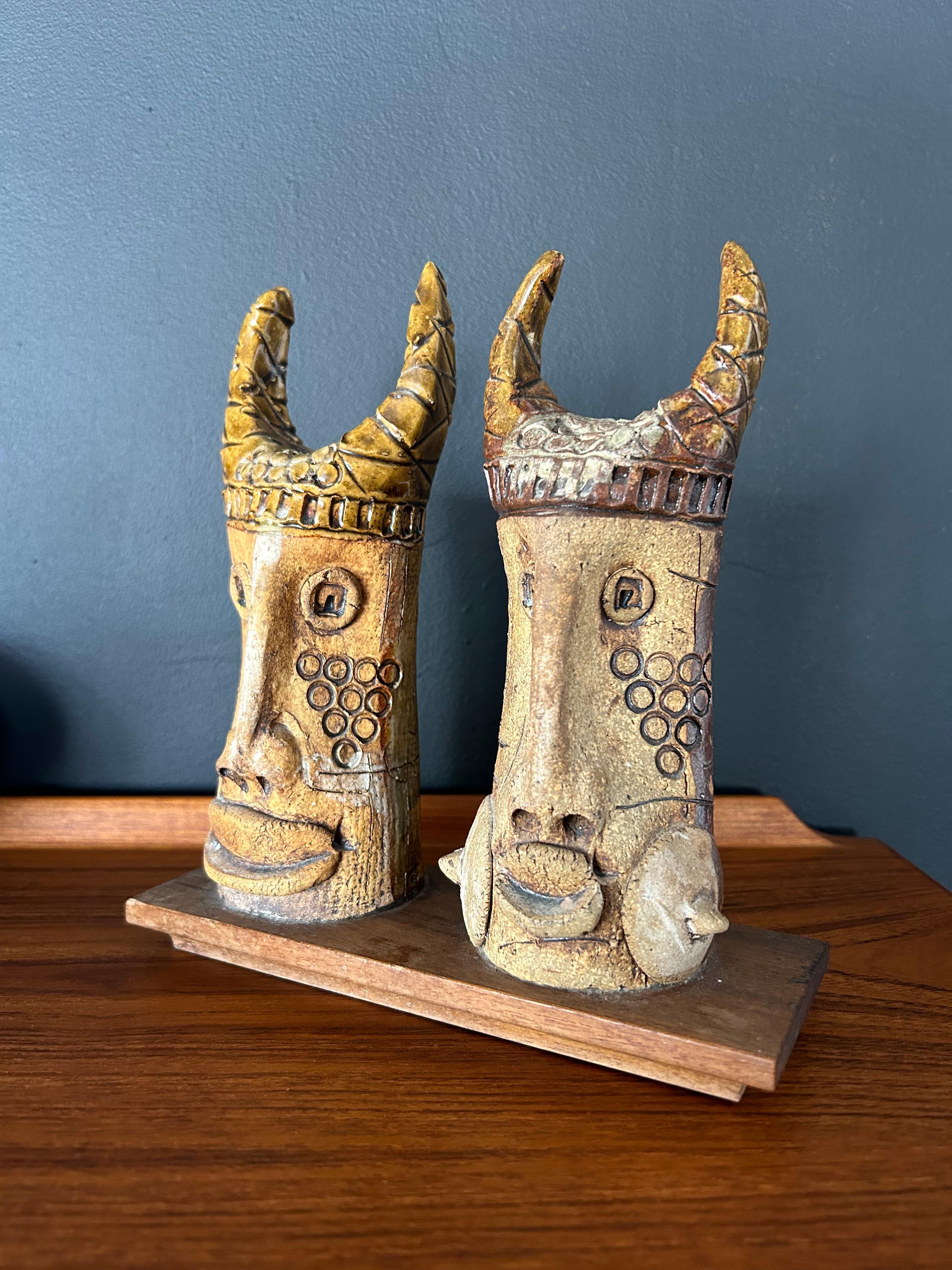 Skurriles Paar Wikingergesichter aus Keramik auf einem Holzsockel, geschaffen vom Künstler Hal Fromhold. Das Kunstwerk enthält ein handgeschriebenes Label auf der Unterseite mit der Aufschrift 